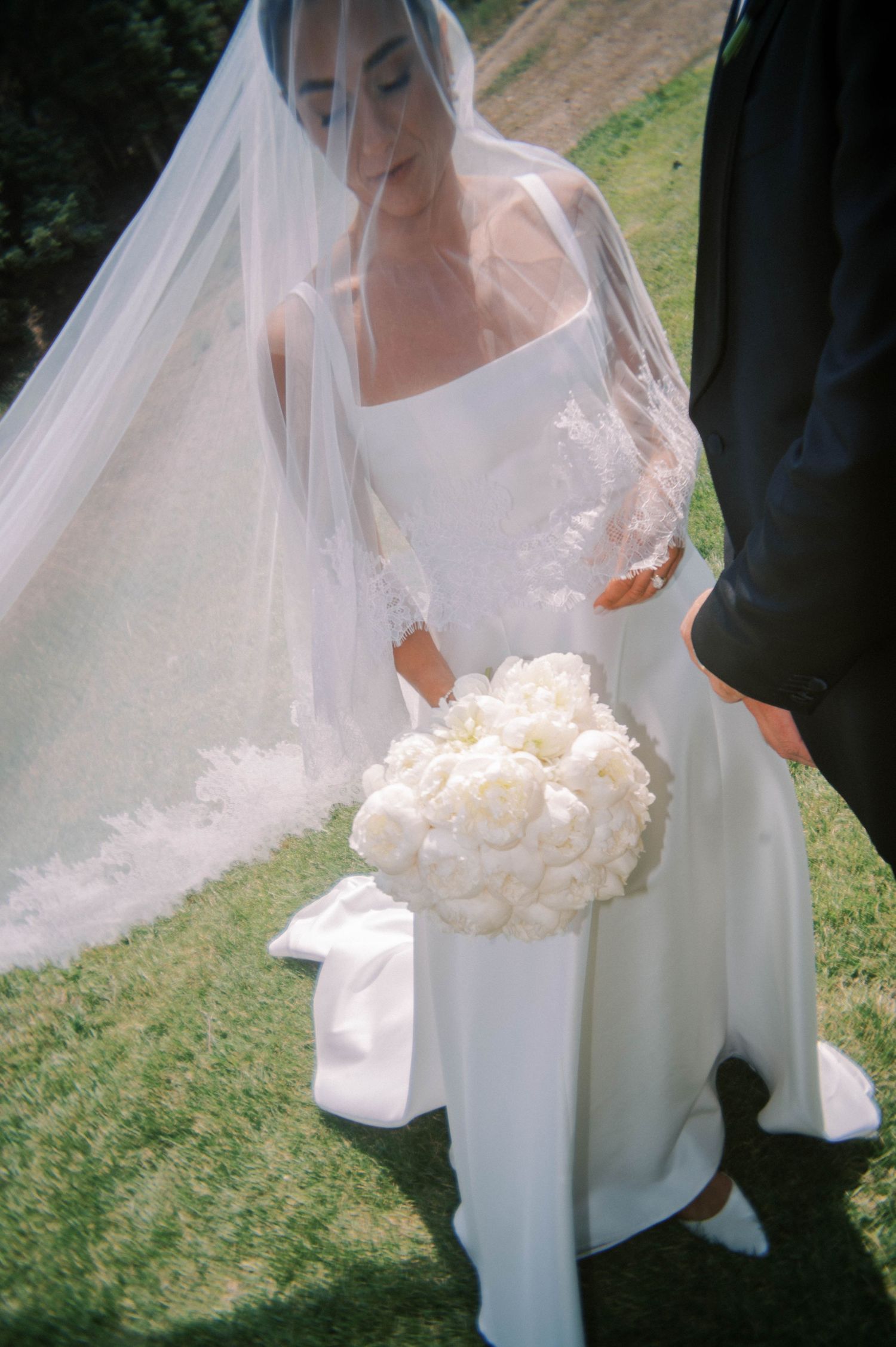 A white wedding bouquet and dress details shown against a natural outdoor backdrop.