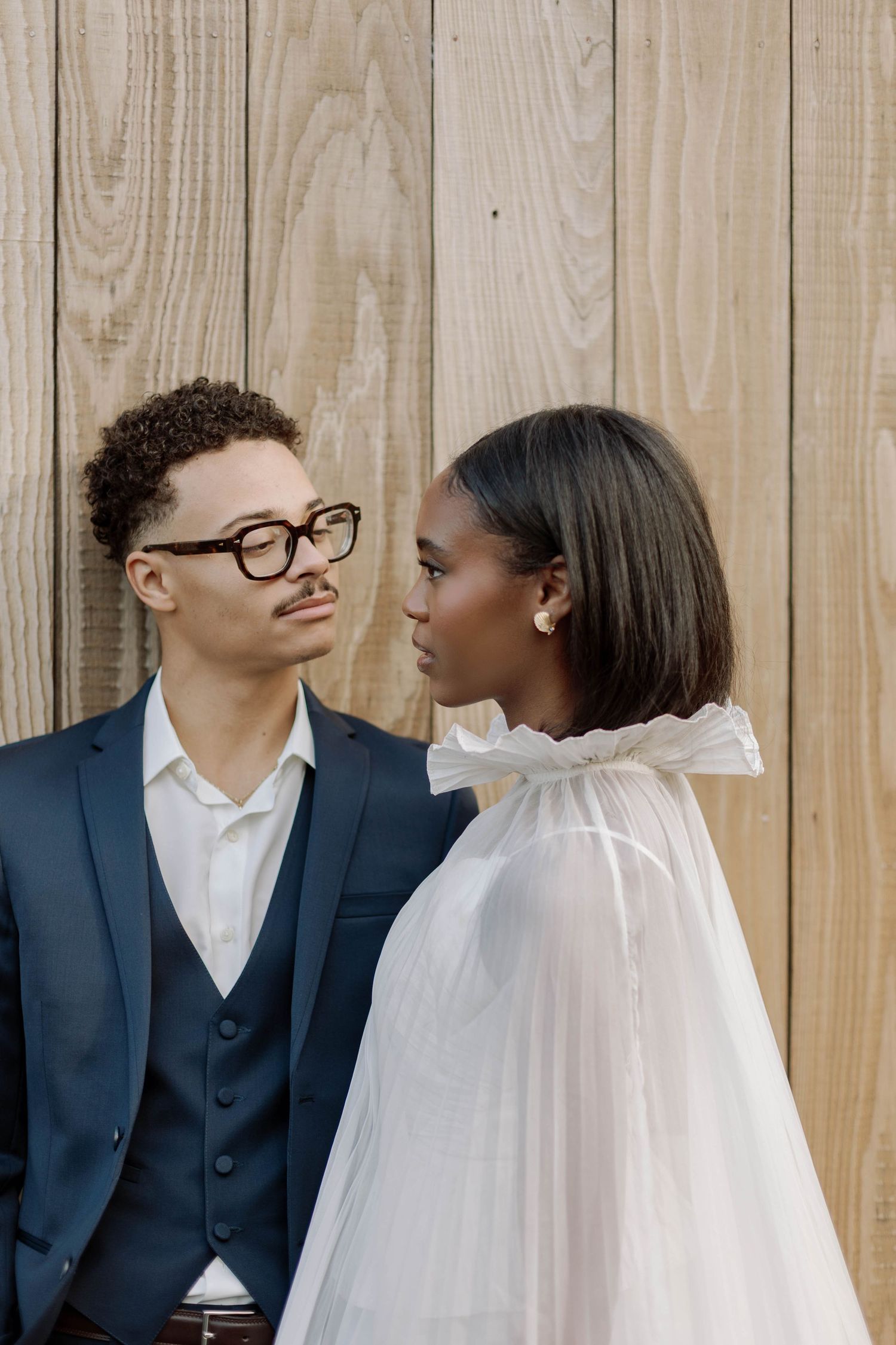 A couple in wedding attire shares an intimate moment against a wooden wall backdrop.