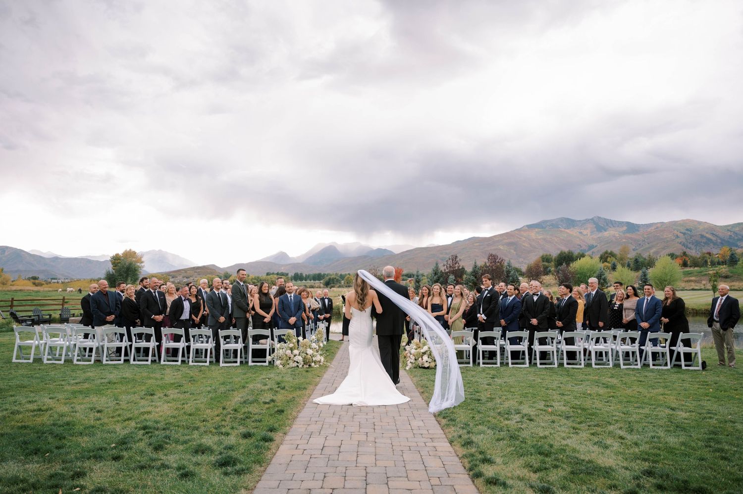 Wedding ceremony setup with white chairs arranged outdoors against a backdrop of scenic mountains and cloudy skies.