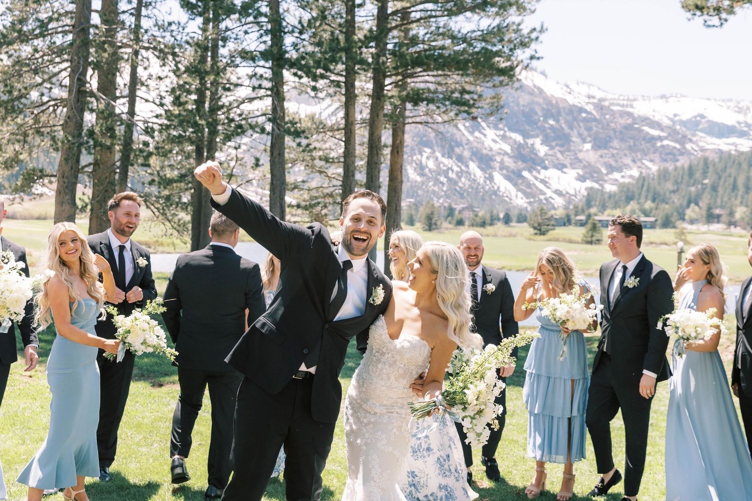 Joyful celebration moment with wedding party in a mountain meadow setting.