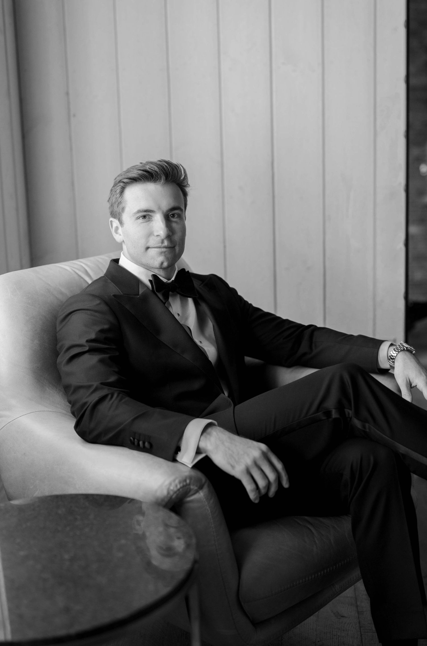 Artistic black and white photograph showing person reclining in formal attire on modern furniture.