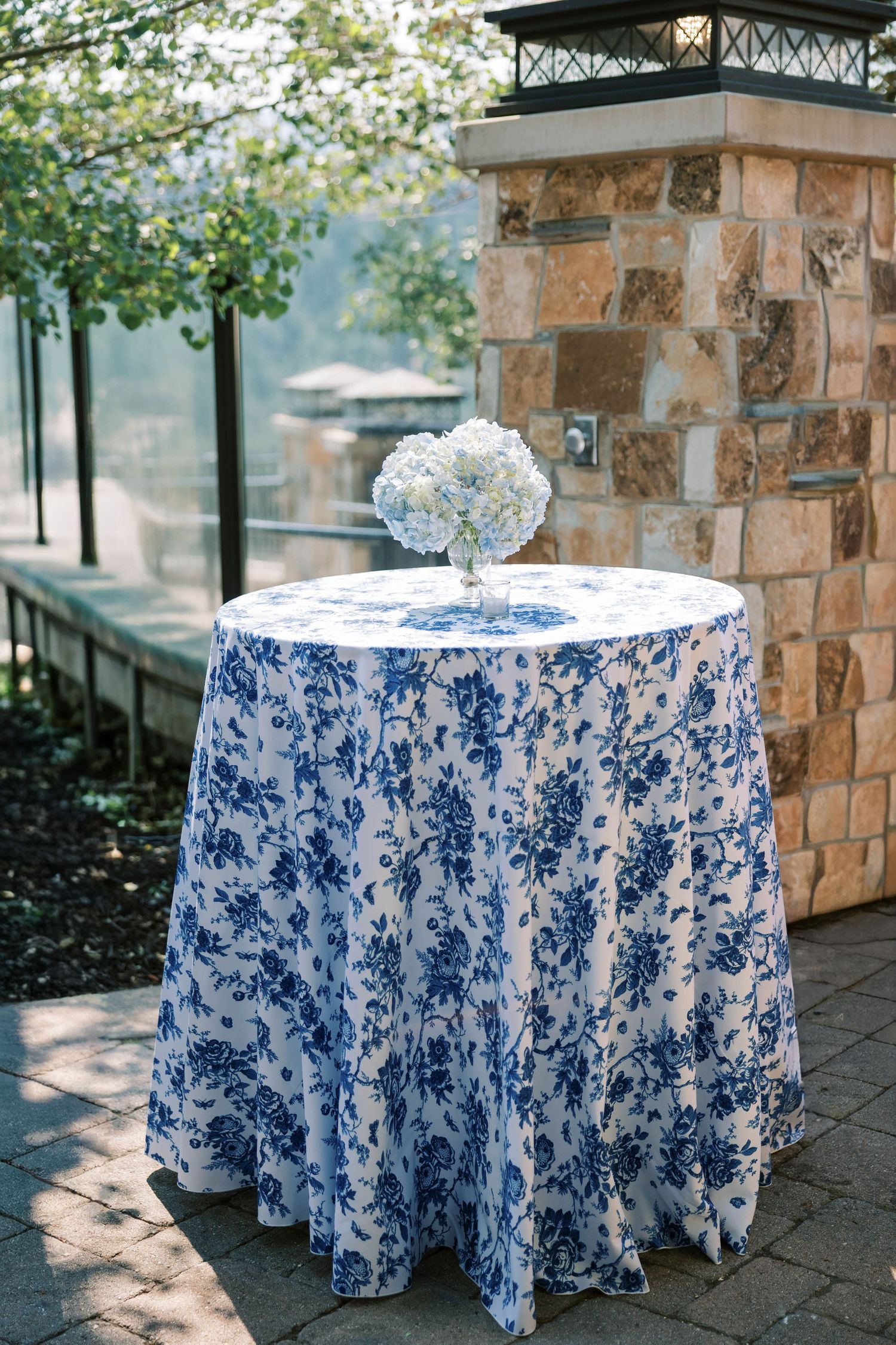 Round tables with blue and white floral patterned tablecloths arranged on a stone patio.