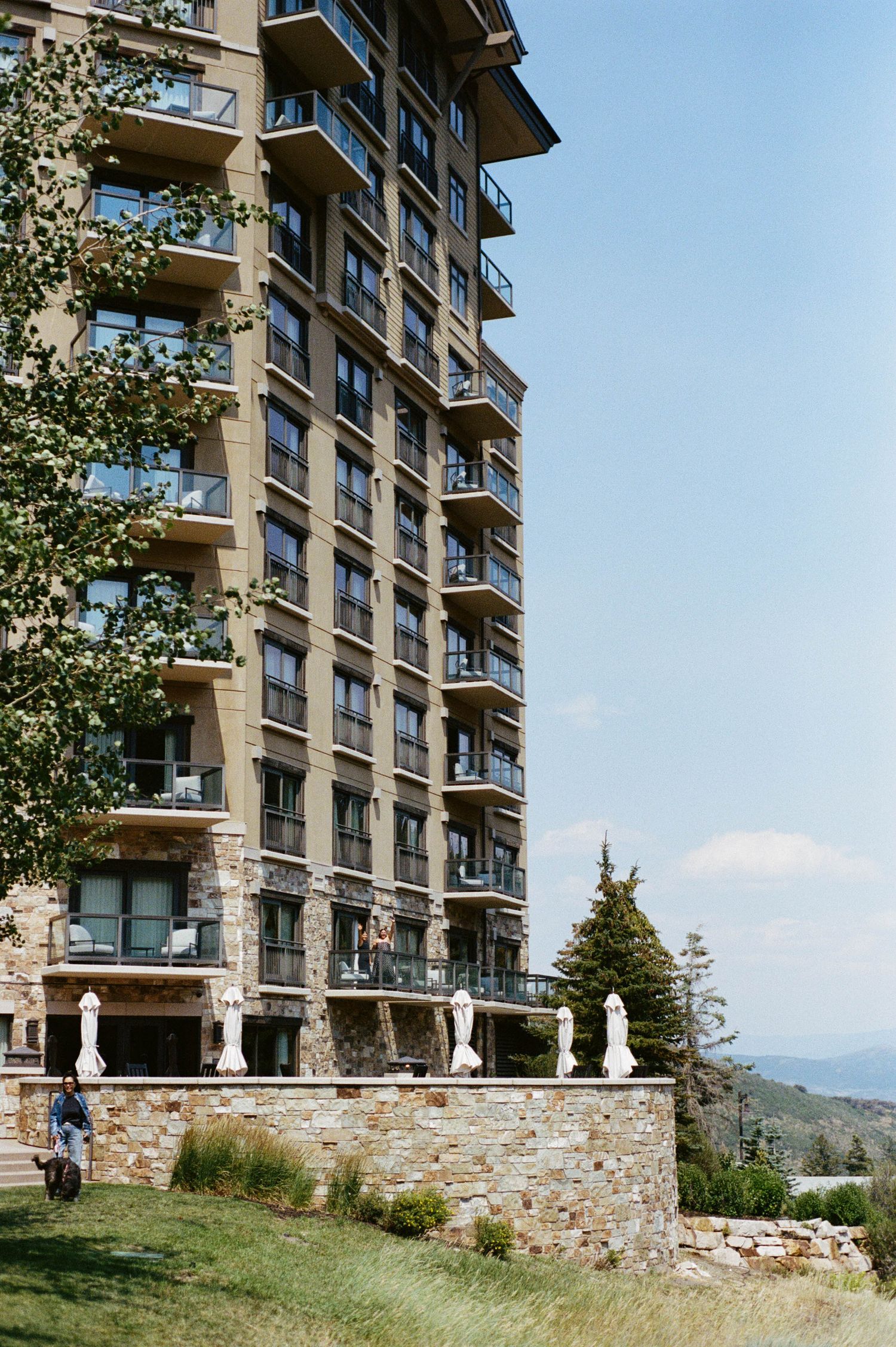 Modern luxury apartment building with stone facade and balconies overlooking scenic mountain landscape.