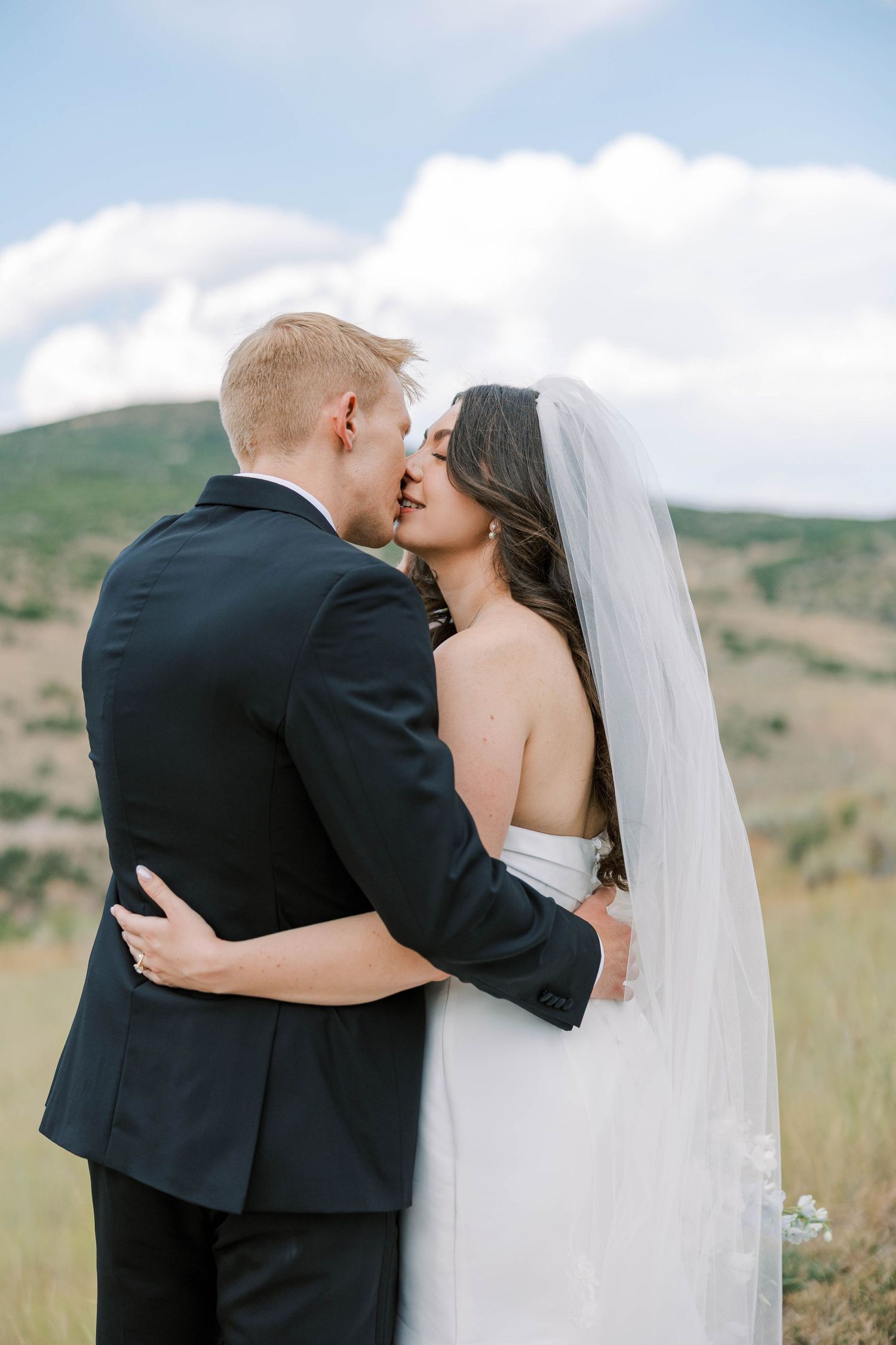 A romantic outdoor wedding moment captured against rolling hills and blue sky.