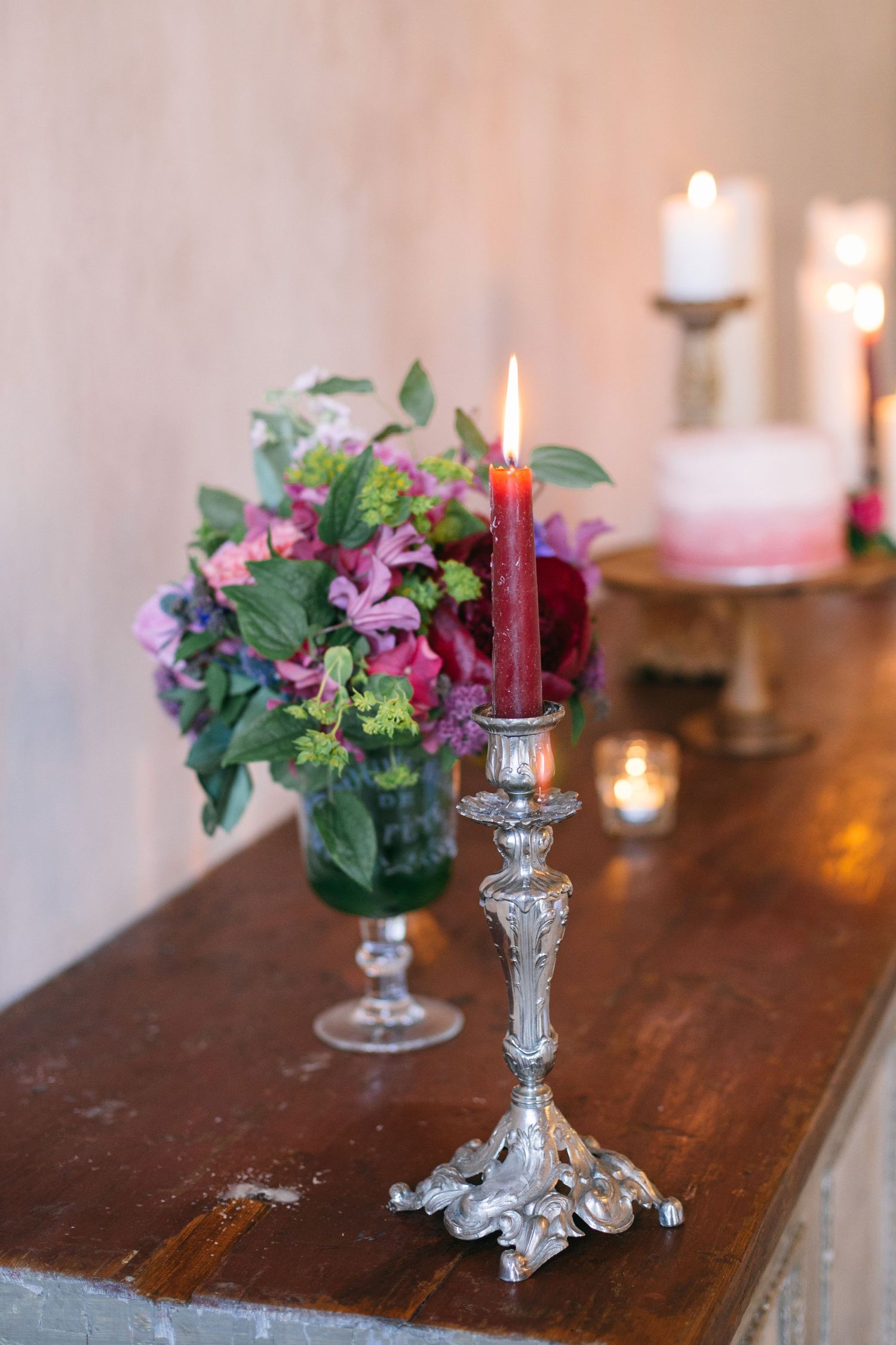 Ornate silver candlestick with red taper candle beside purple floral arrangement.