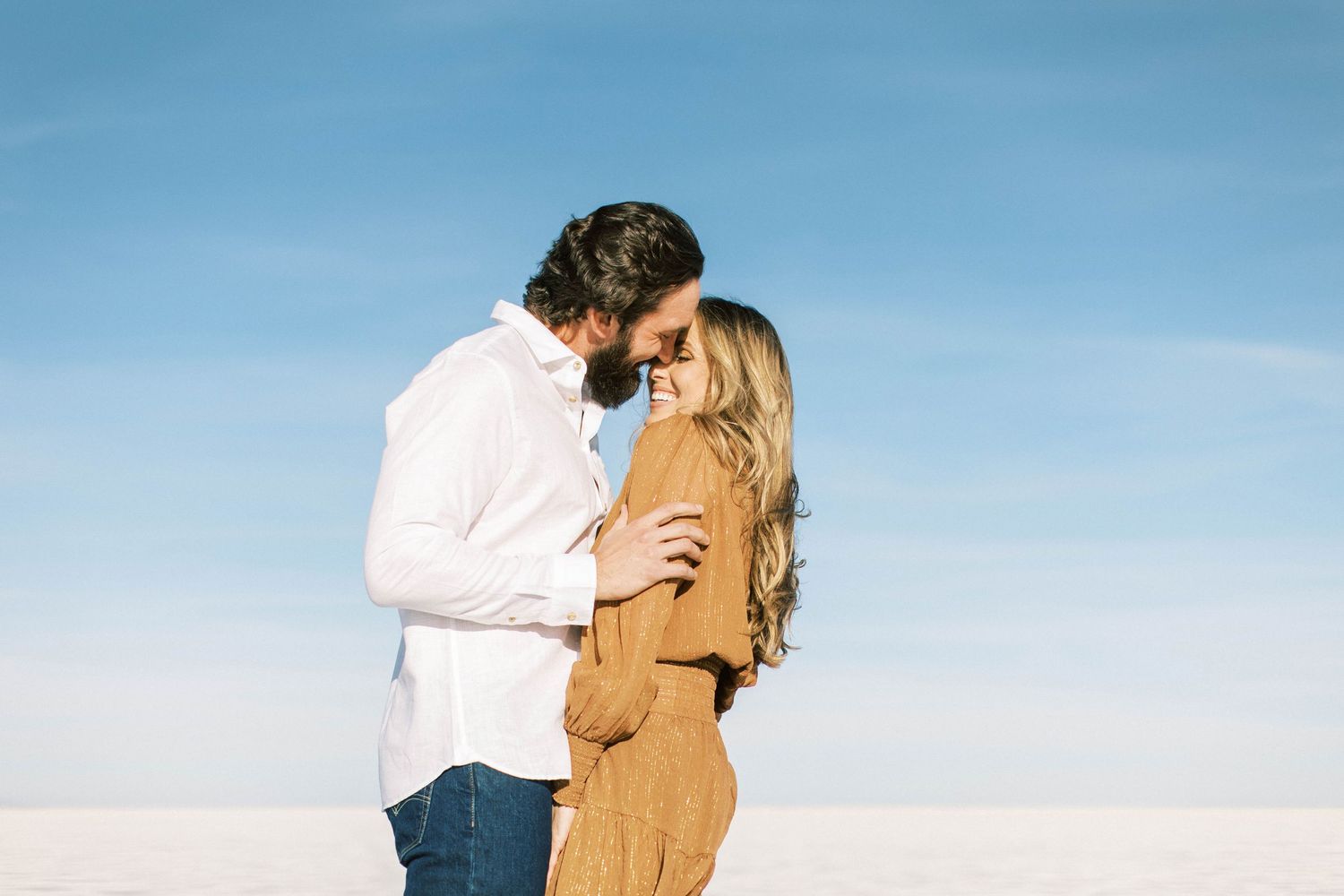 Romantic moment between couple in white shirt and camel dress on salt flats.