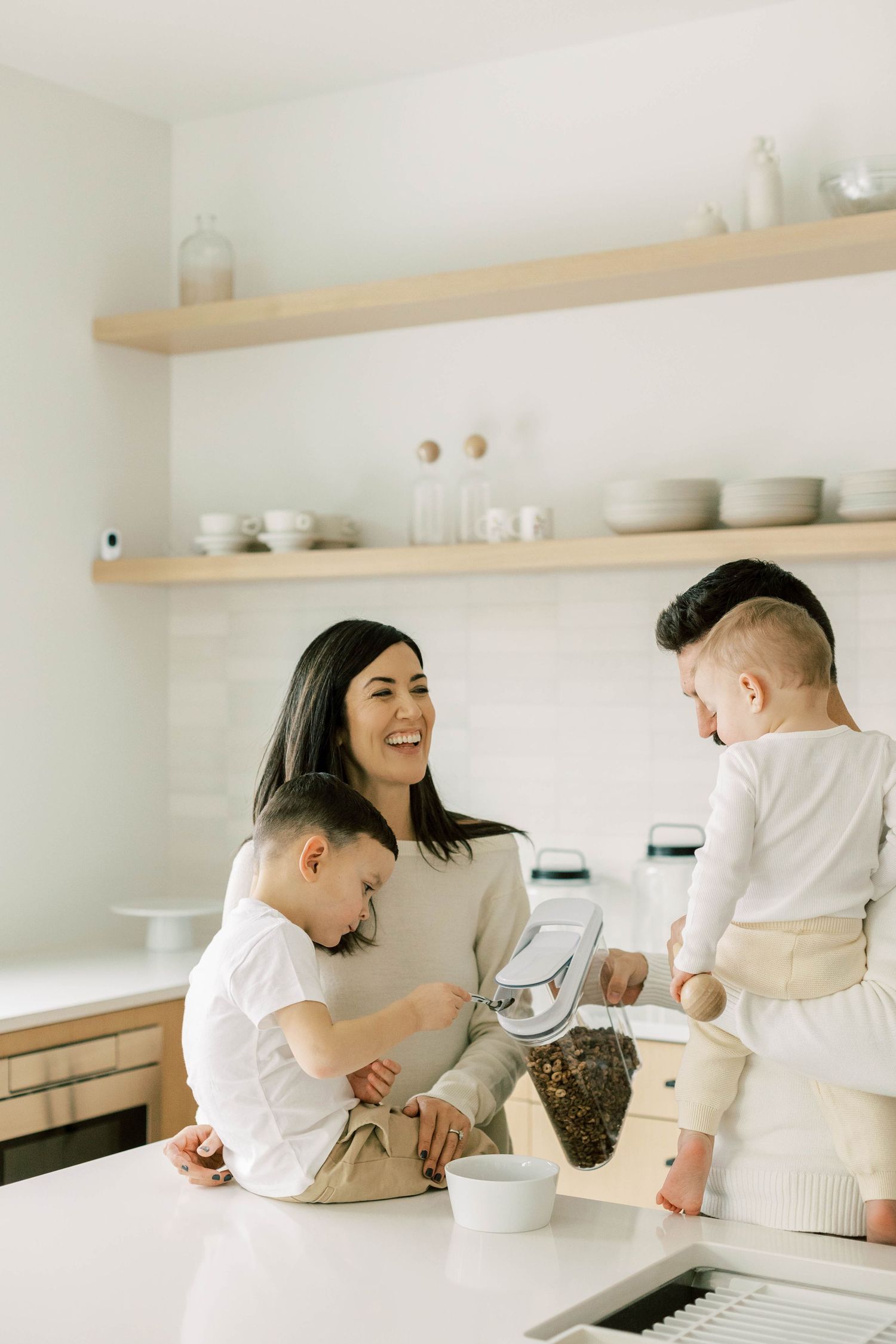 Casual family moment in modern white kitchen with floating shelves and minimal decor.