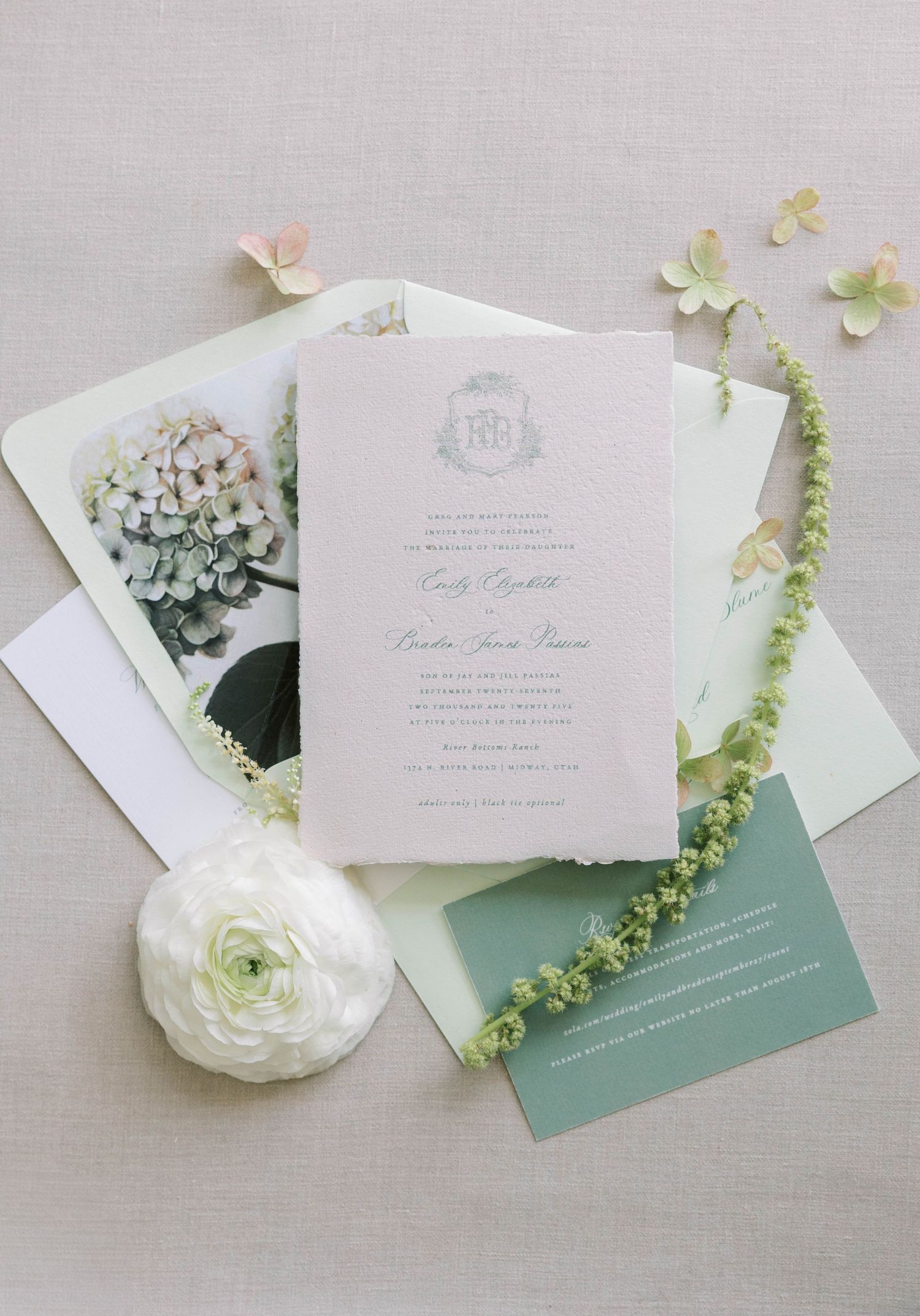 Elegant wedding invitations with sage green accents and white flowers arranged on light gray background.