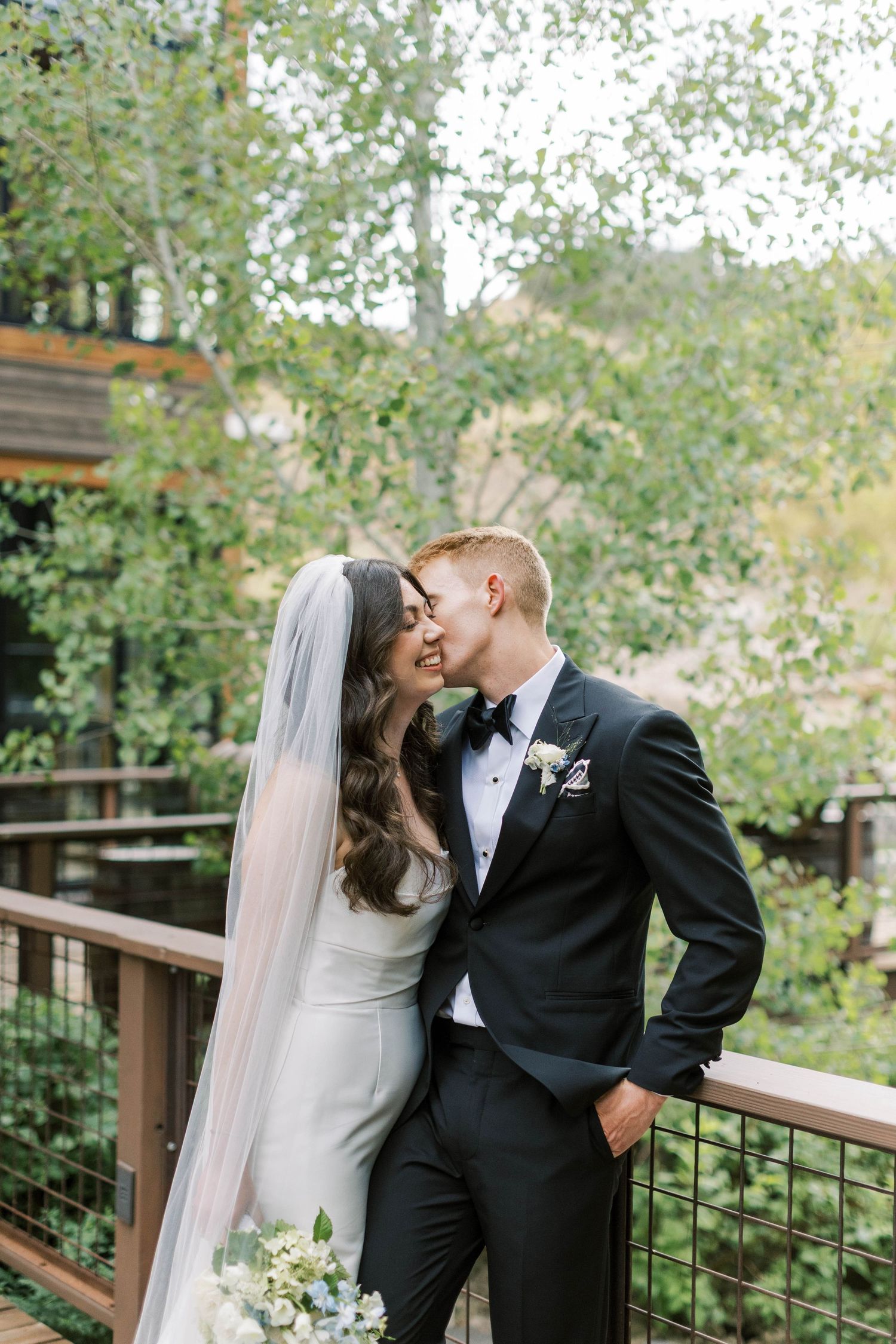 Romantic wedding couple sharing intimate moments on a wooden deck surrounded by greenery.