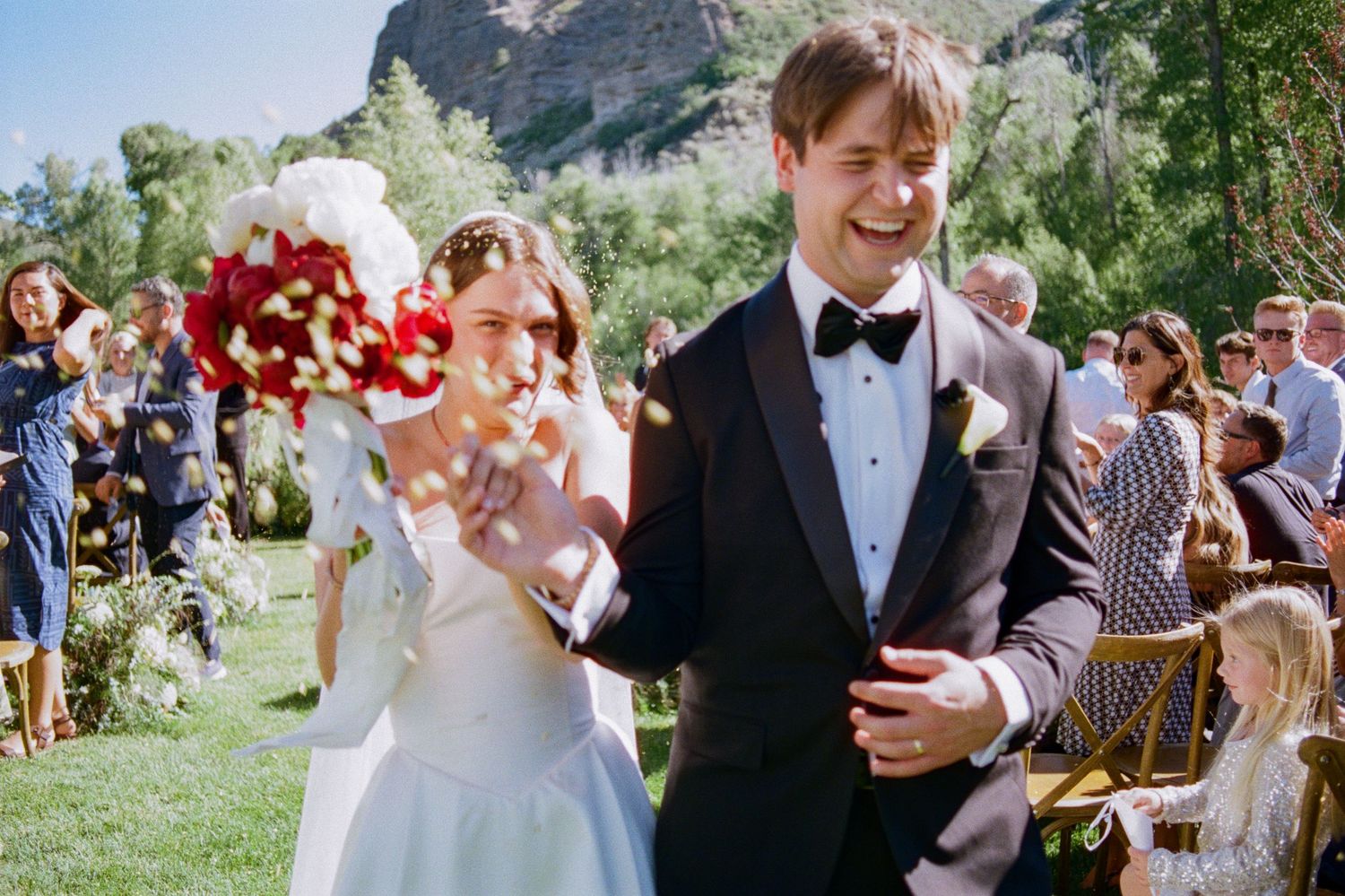 Wedding guests celebrate outdoors at a summer garden reception with confetti and champagne.