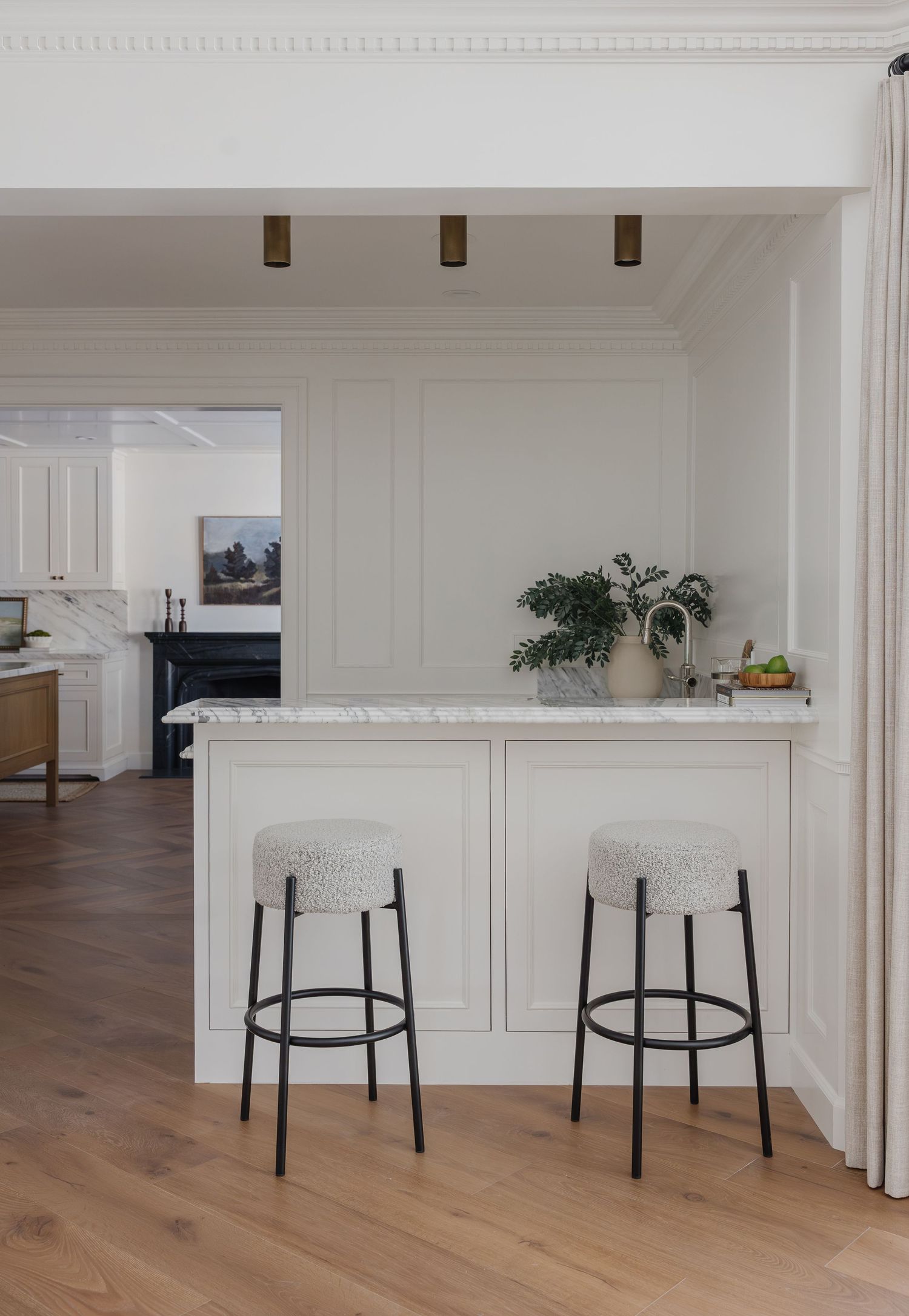 Elegant white kitchen peninsula with marble countertop, two boucle bar stools, and warm wood floors in a classic interior.