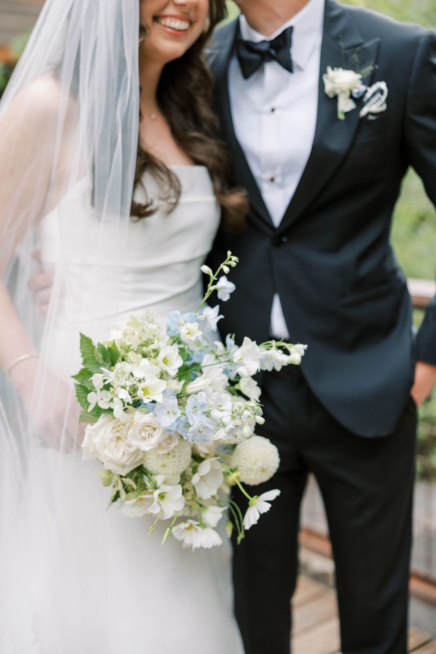 Elegant white bridal bouquet with delicate flowers and greenery against formal wedding attire.