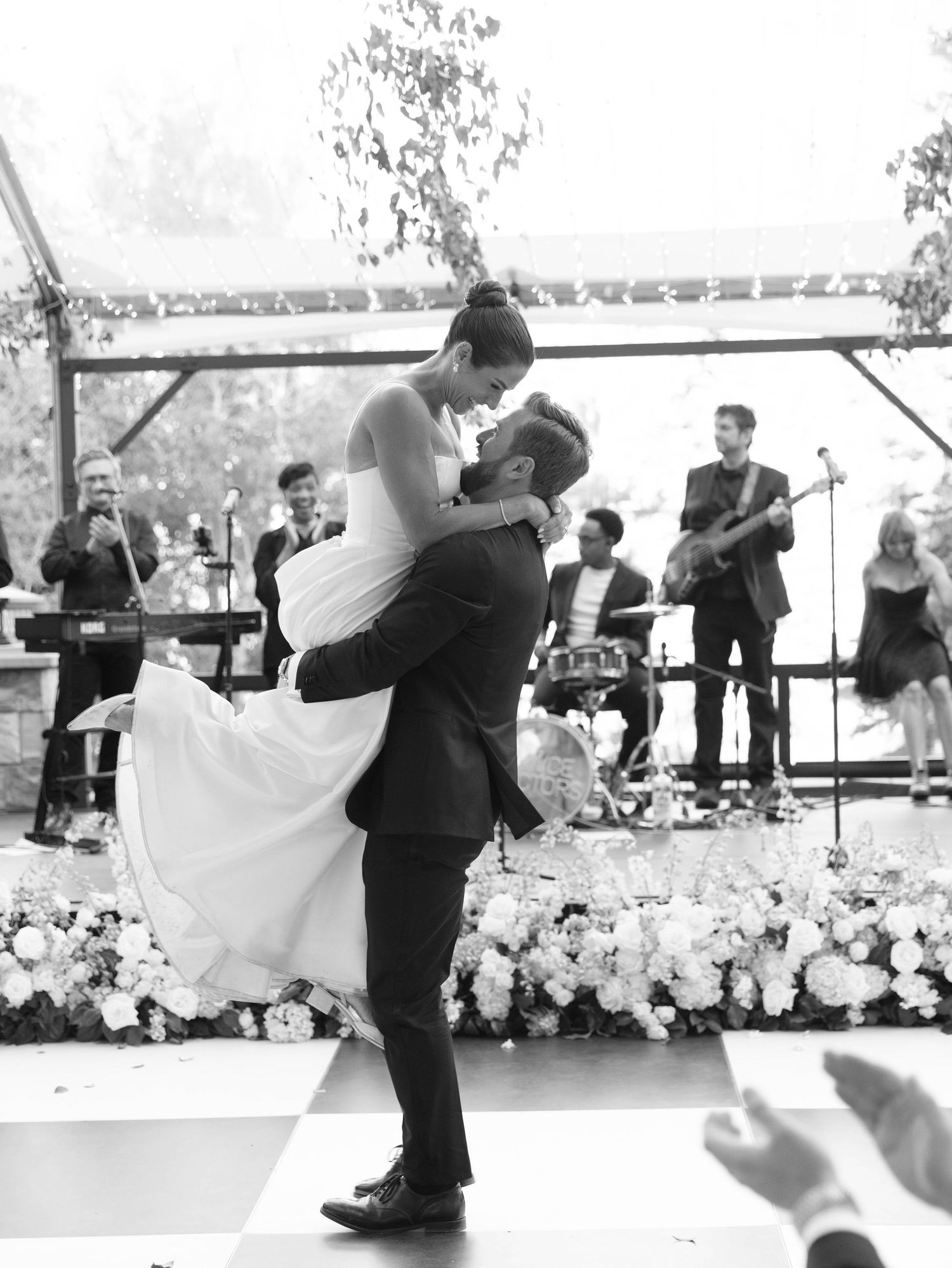 A couple performs a romantic dance dip during their first dance at a wedding reception with floral decorations.