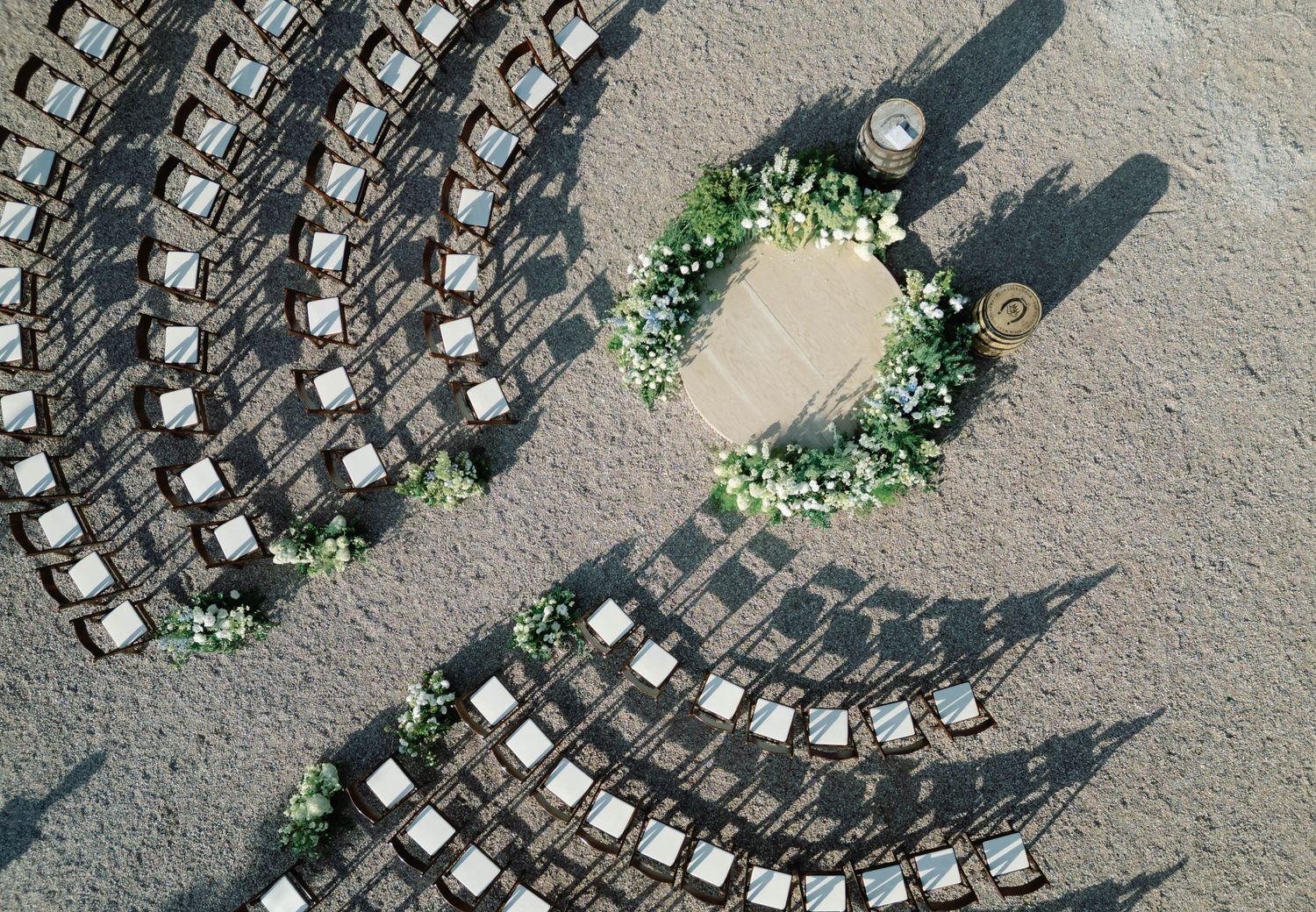 Aerial view of empty chairs arranged in curved rows on a gravel surface with scattered greenery around the edges.