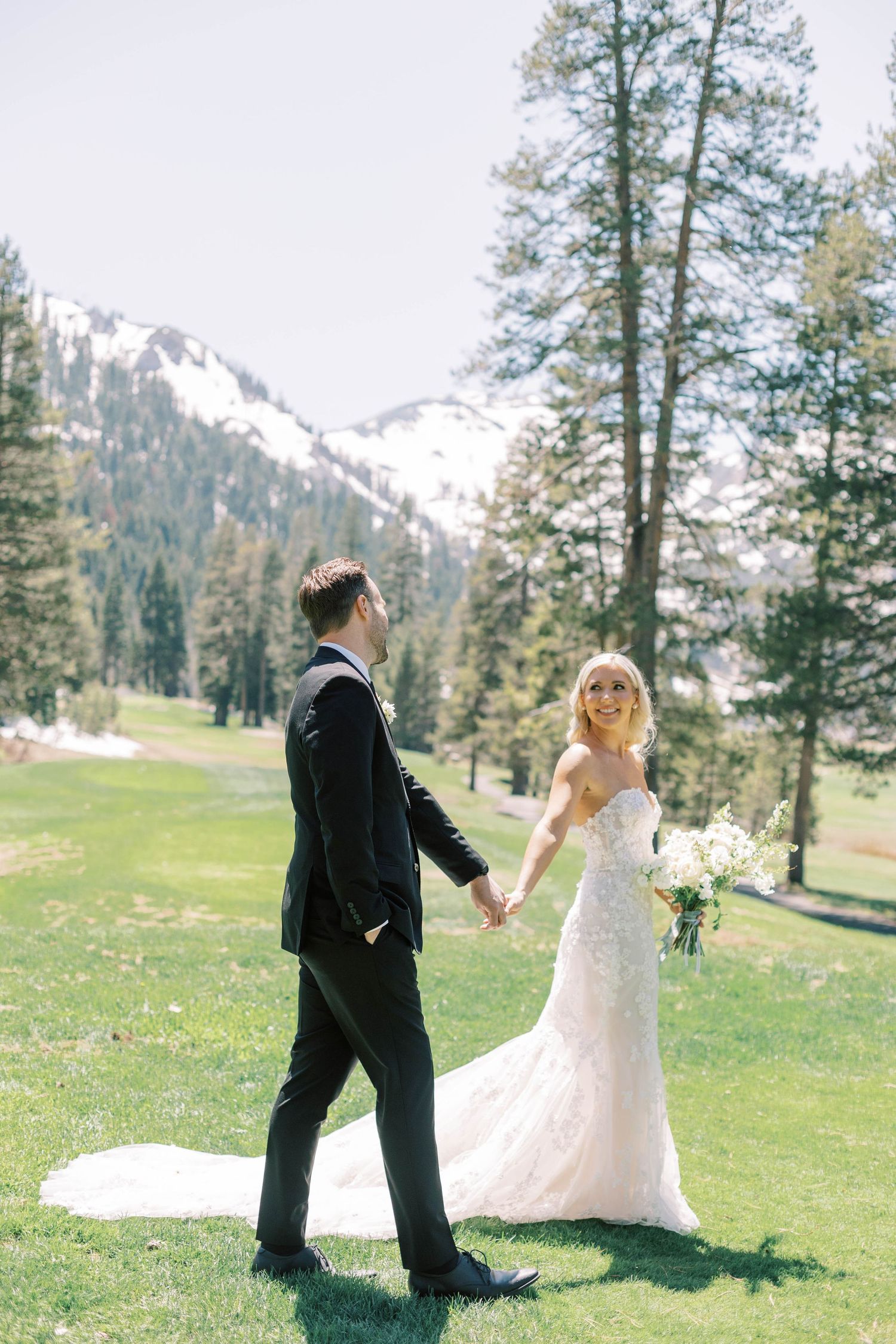 A wedding couple poses in a scenic mountain meadow surrounded by tall pine trees and snowy peaks at everline resort in lake tahoe.