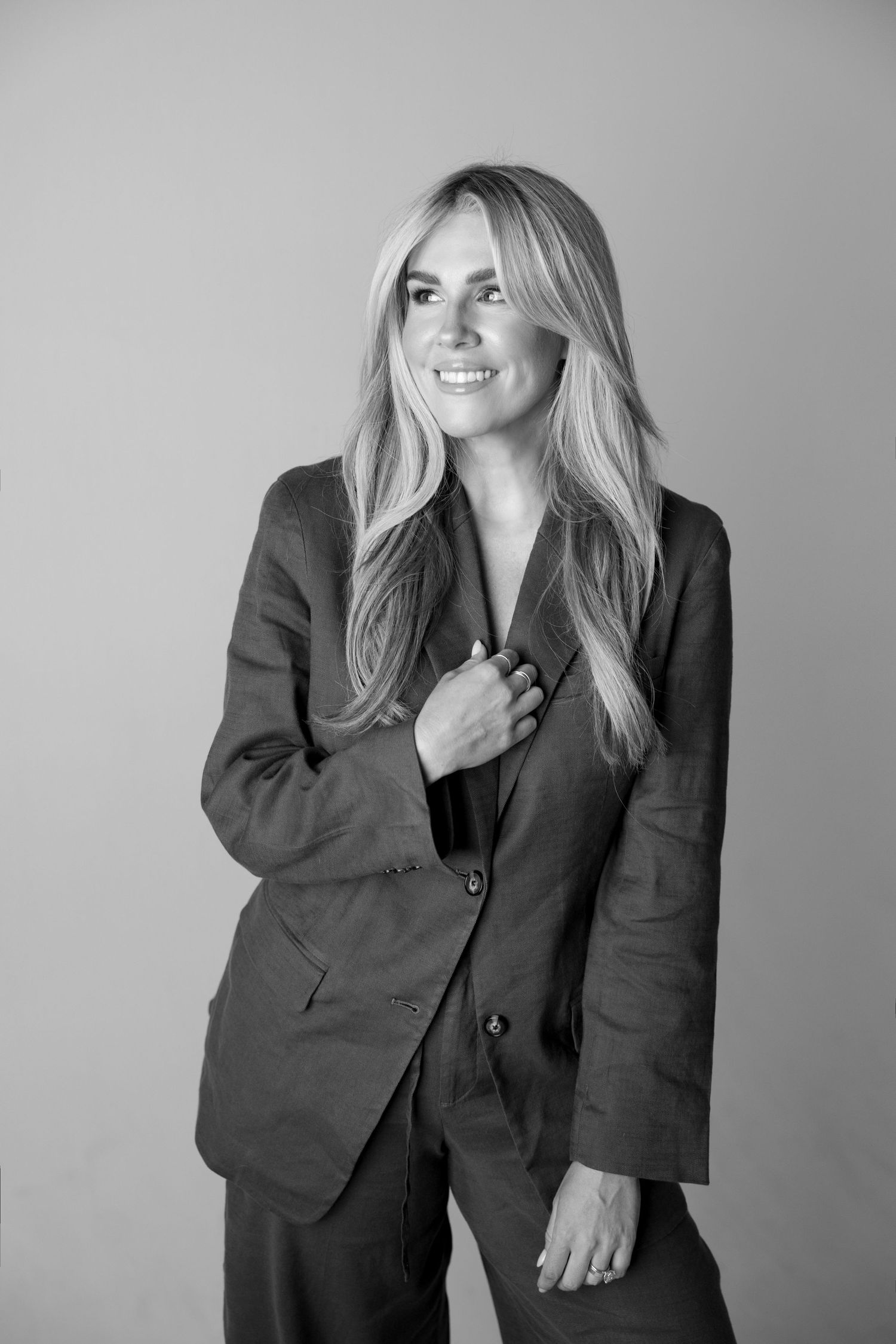Smiling blonde woman in a tailored suit posing confidently in a black and white professional portrait photo.