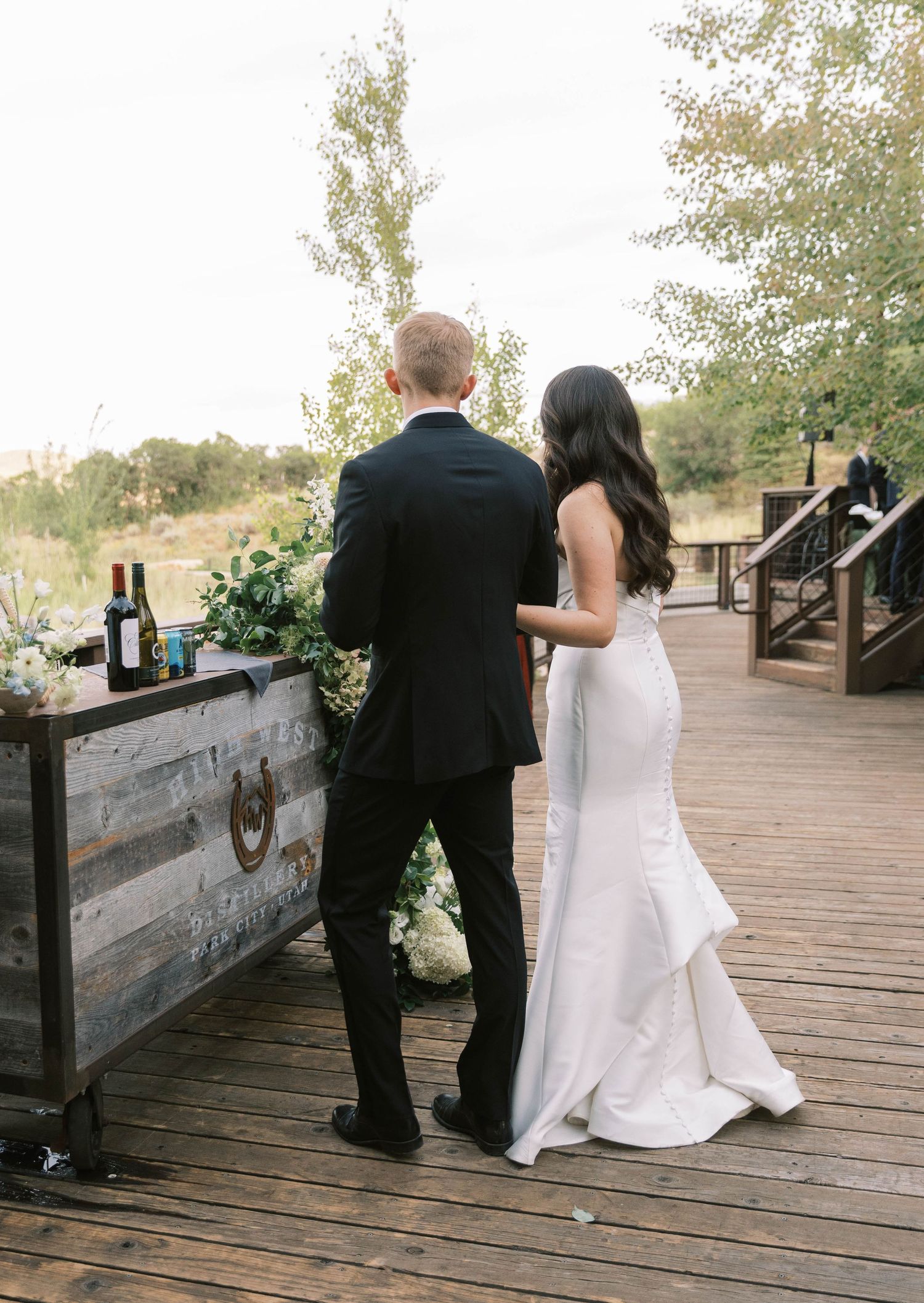 Wedding couple walking along a rustic wooden boardwalk in an outdoor setting.