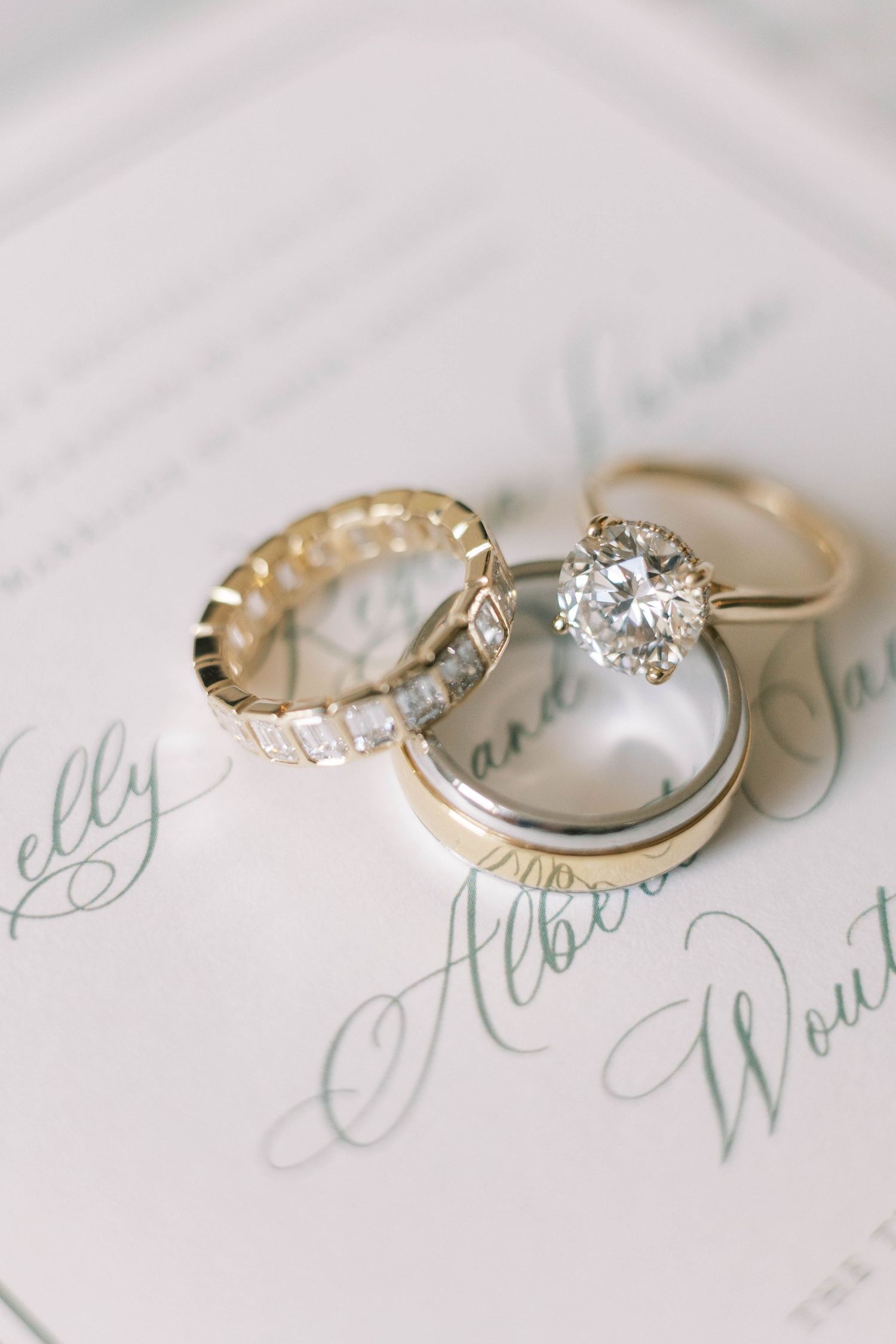 Elegant diamond engagement rings and wedding bands arranged on white paper with calligraphy.