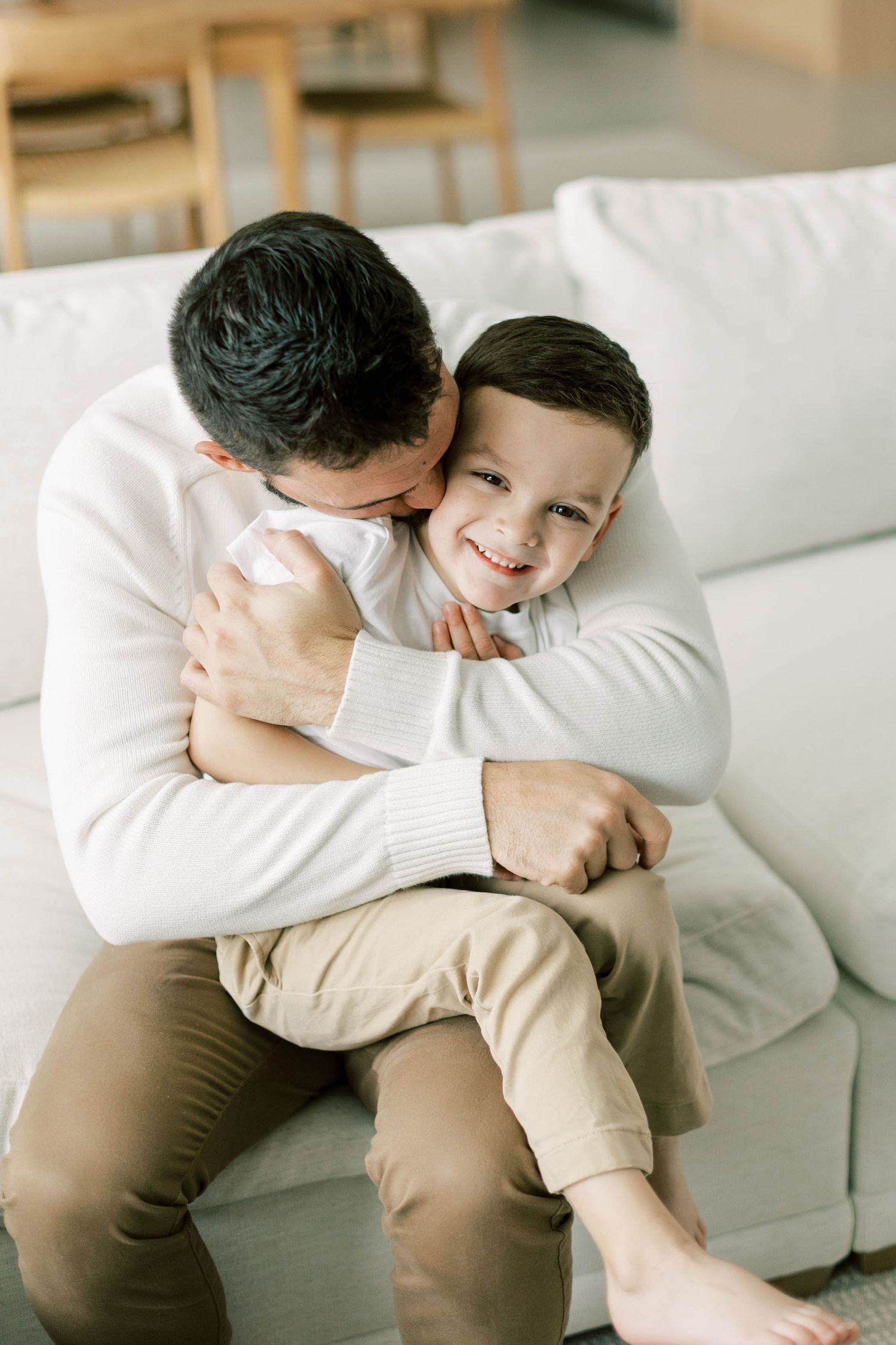 Playful embrace between parent and child on white sofa in bright interior setting.