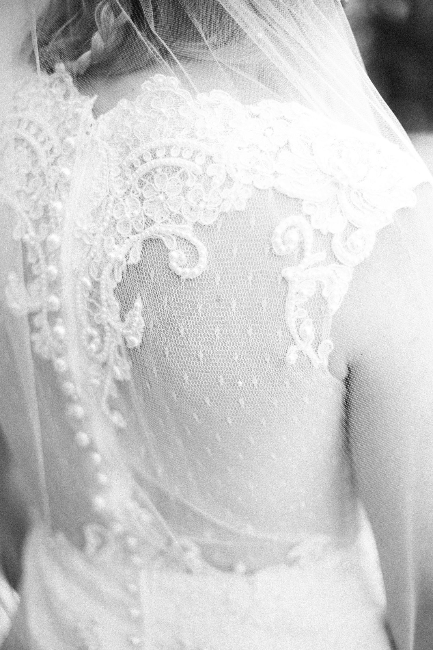 Close-up detail of intricate lace pattern on a white wedding dress bodice in black and white.