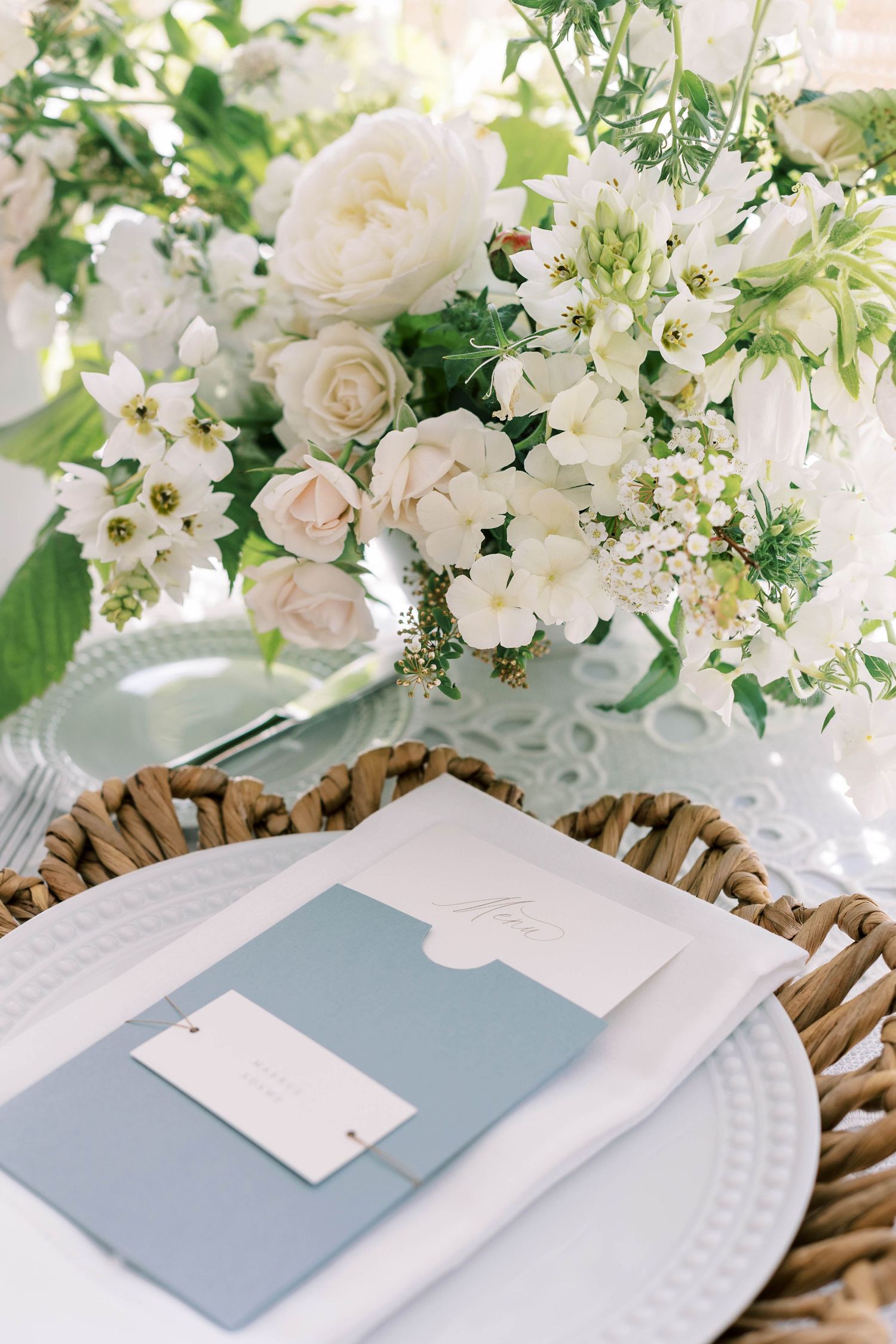 Romantic white floral arrangement with roses and greenery beside a blue wedding menu card at everline resort lake tahoe.