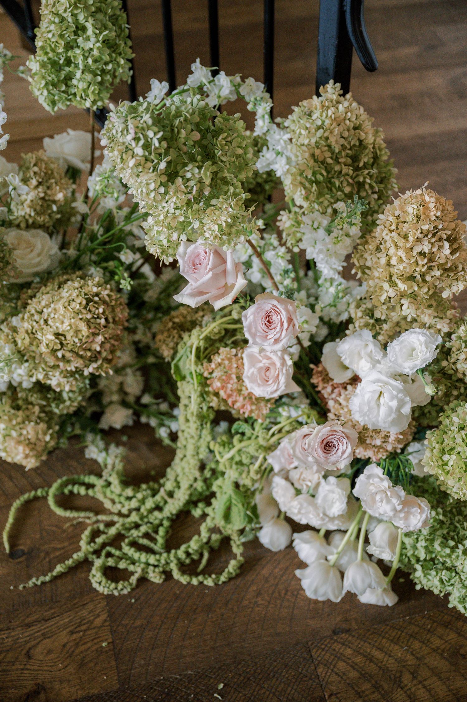 Romantic floral arrangement featuring soft pink roses, white hydrangeas, and cascading greenery on wooden surface.