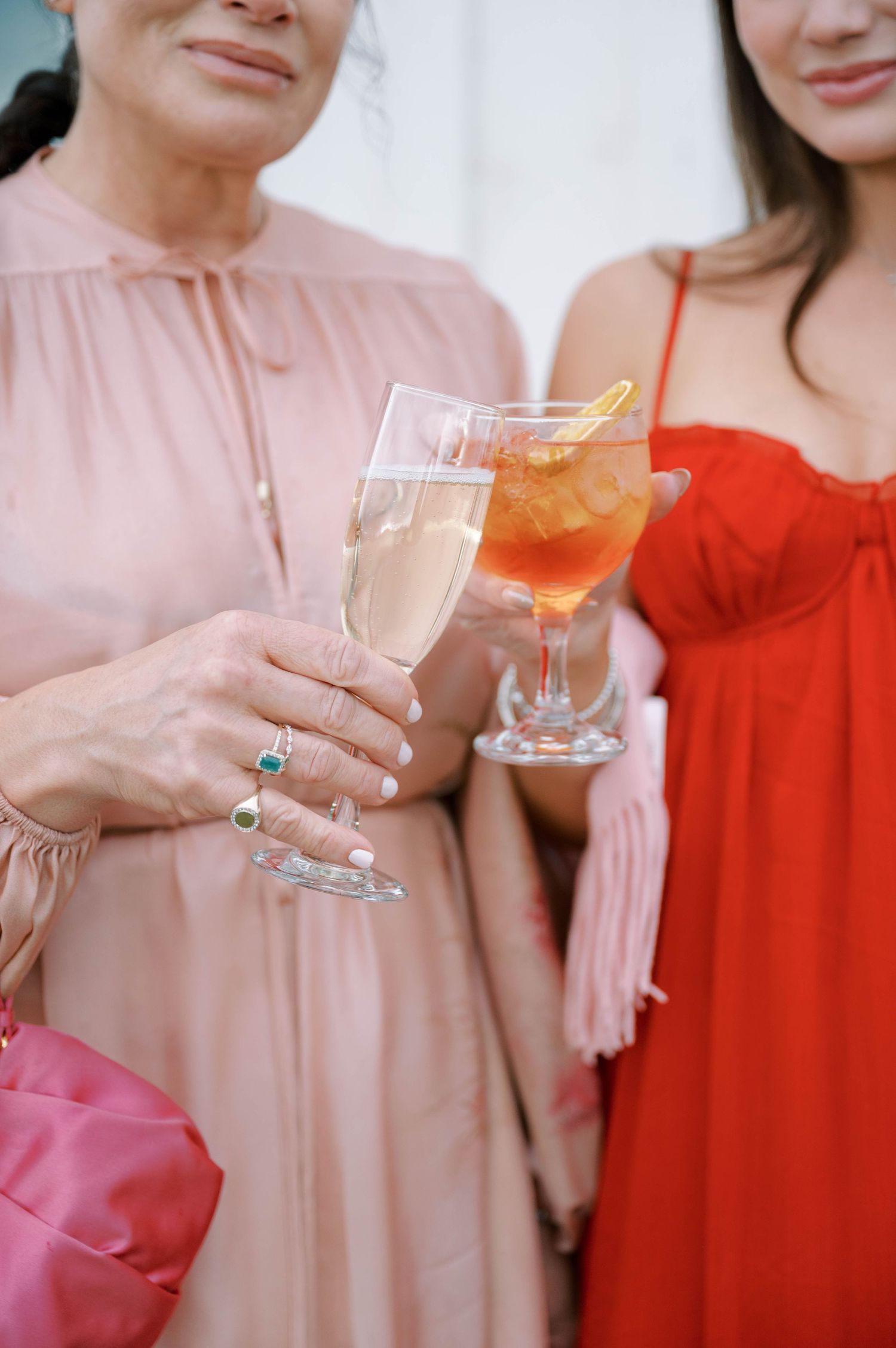 People in pink and red dresses holding champagne glasses for a celebratory toast at an elegant event.