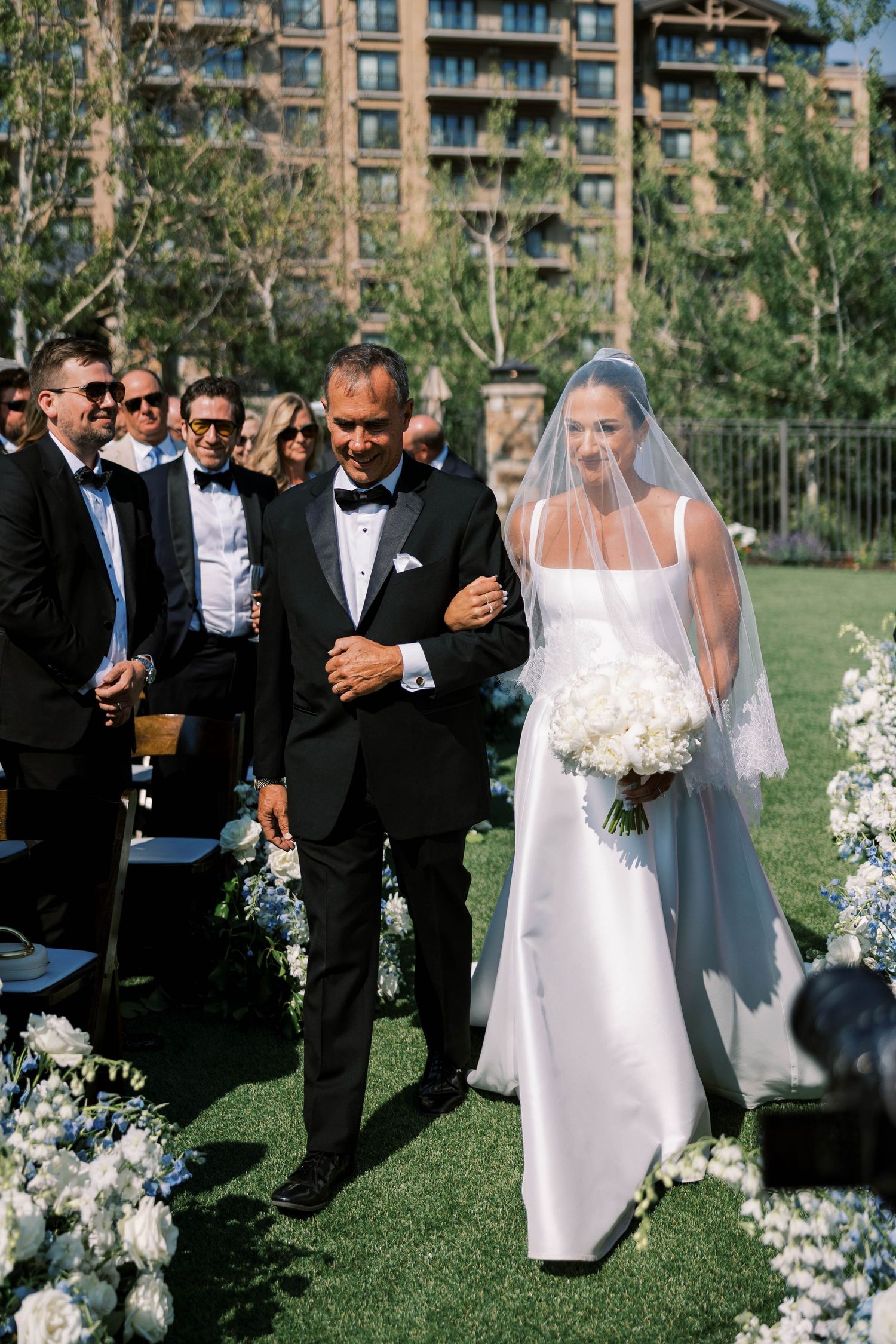 Elegant outdoor wedding ceremony on manicured lawn with floral arrangements and guests in formal attire.