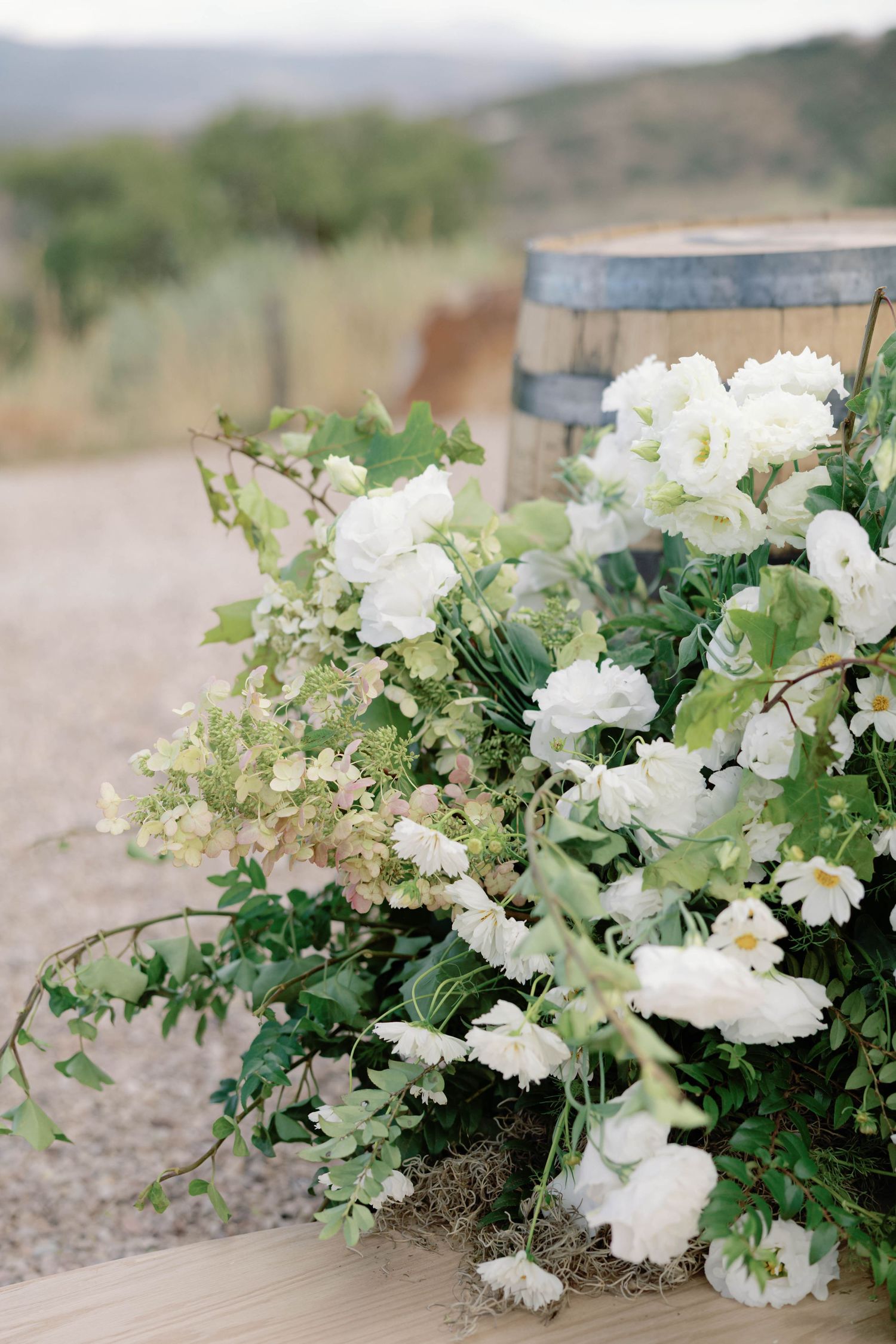Lush white floral arrangements with greenery displayed on rustic outdoor surface.
