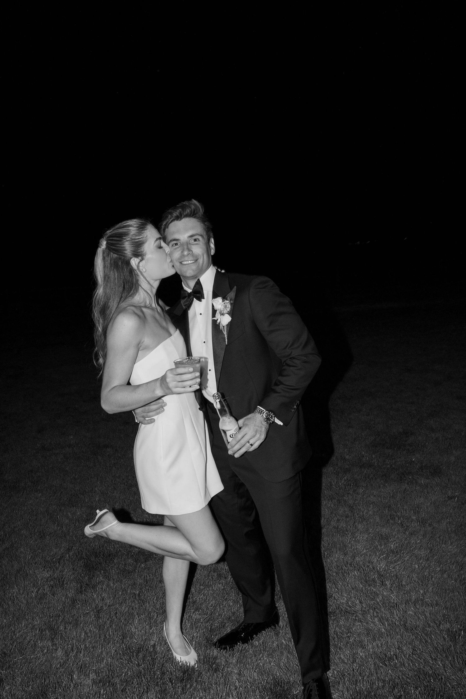 A couple shares a romantic moment together in formal attire on a dark grassy field at night.
