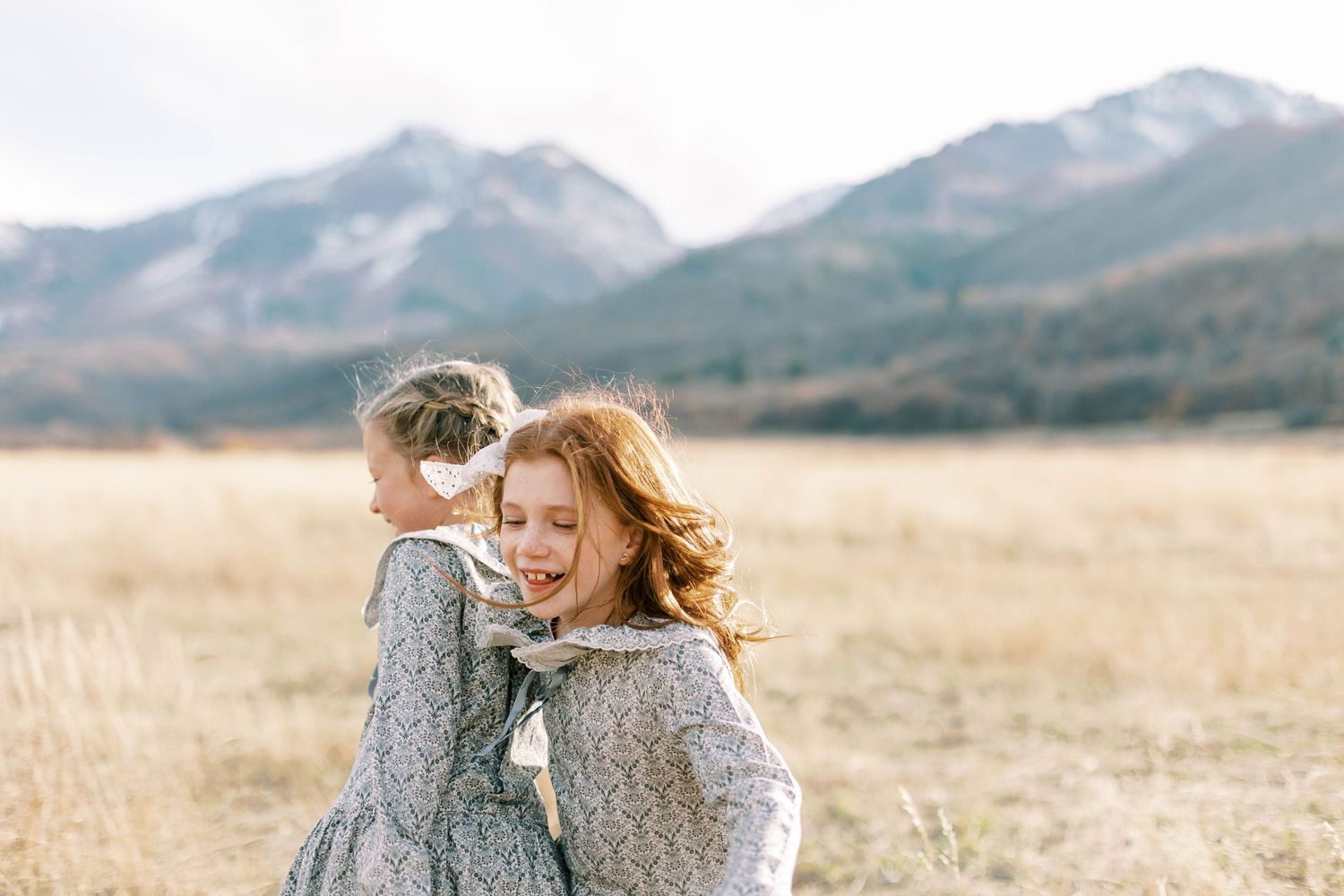 Two people in matching gray dresses laughing together in mountain field.