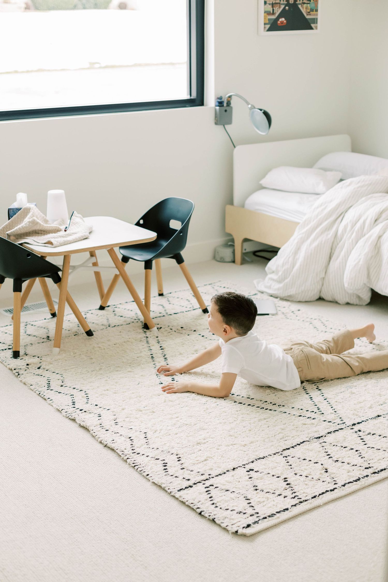 Child lying on patterned rug in modern bedroom with minimalist furniture.