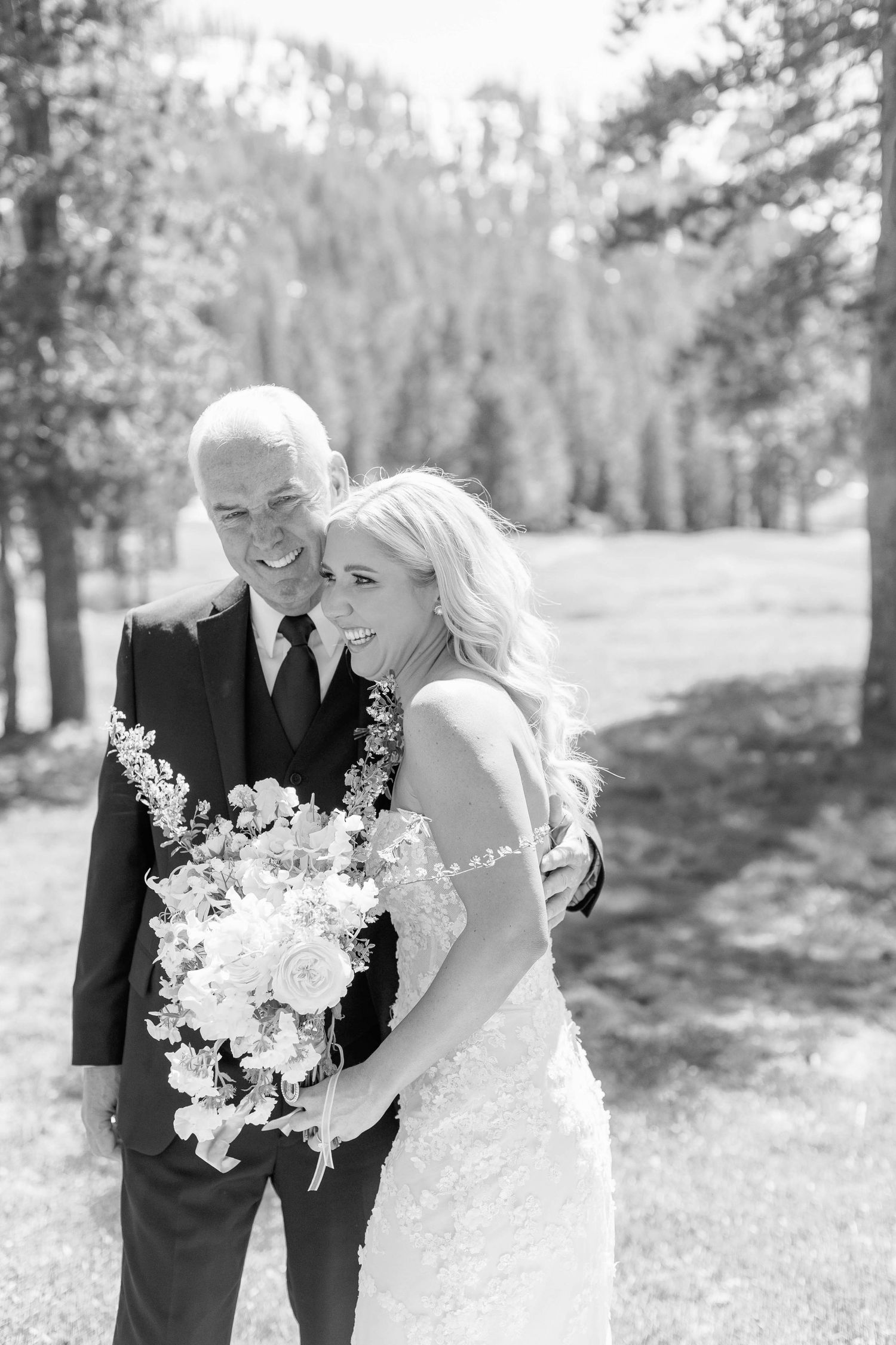 A black and white wedding portrait captured in a serene outdoor mountain setting with pine trees.