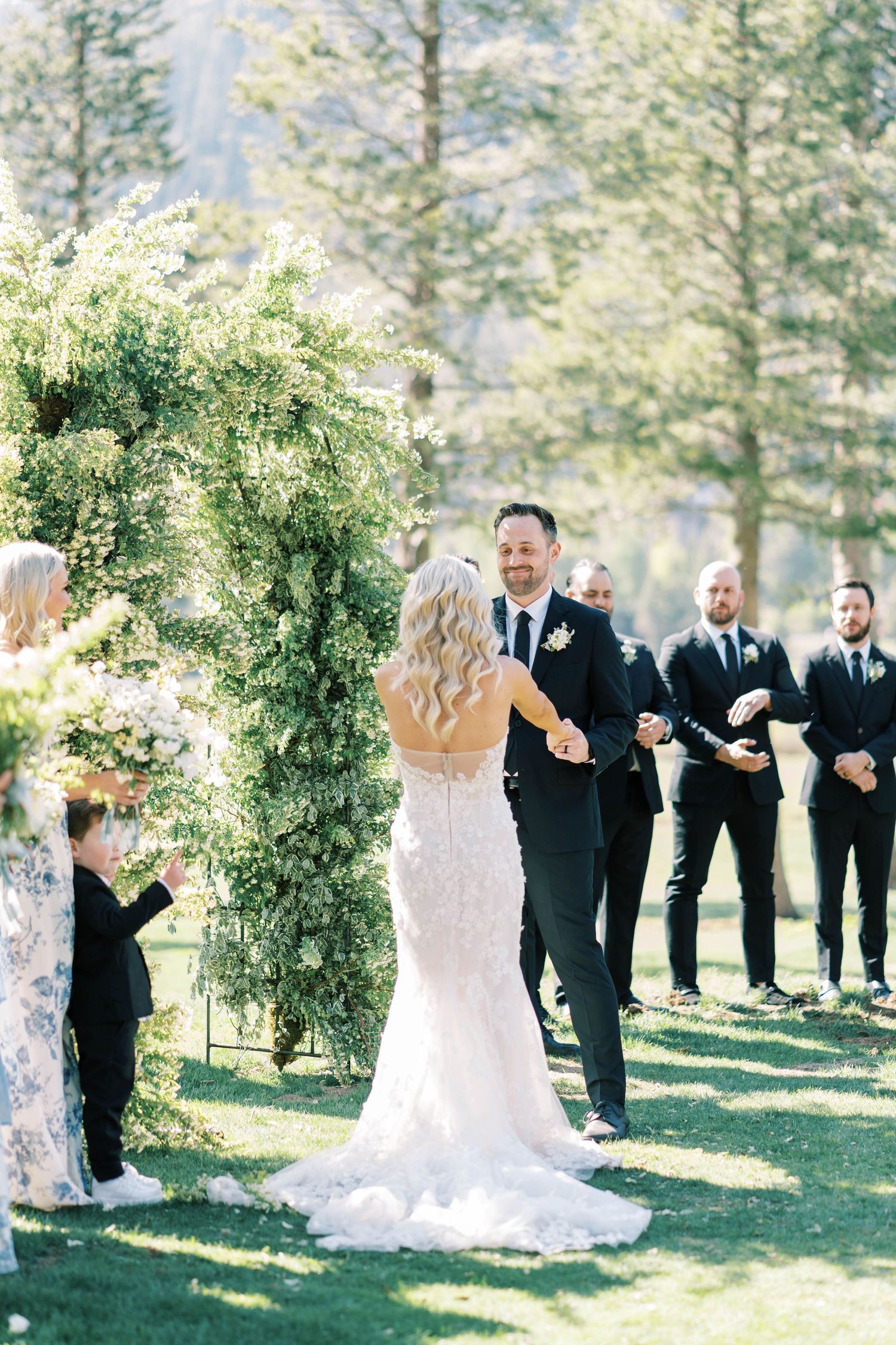 Wedding ceremony under floral arch with mountain backdrop and wedding party.