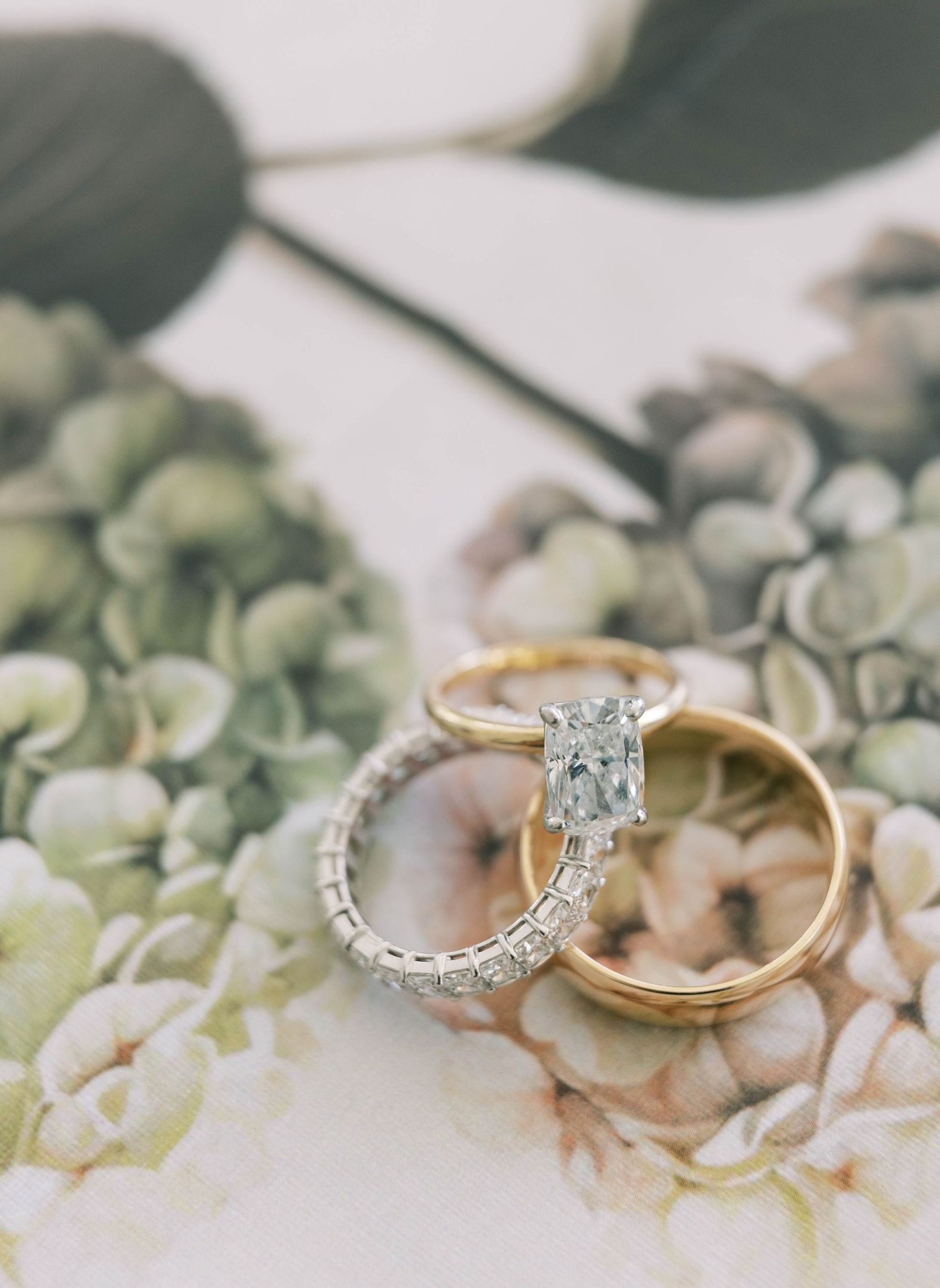 Wedding rings and engagement ring with a sparkling diamond displayed on soft white hydrangea petals.
