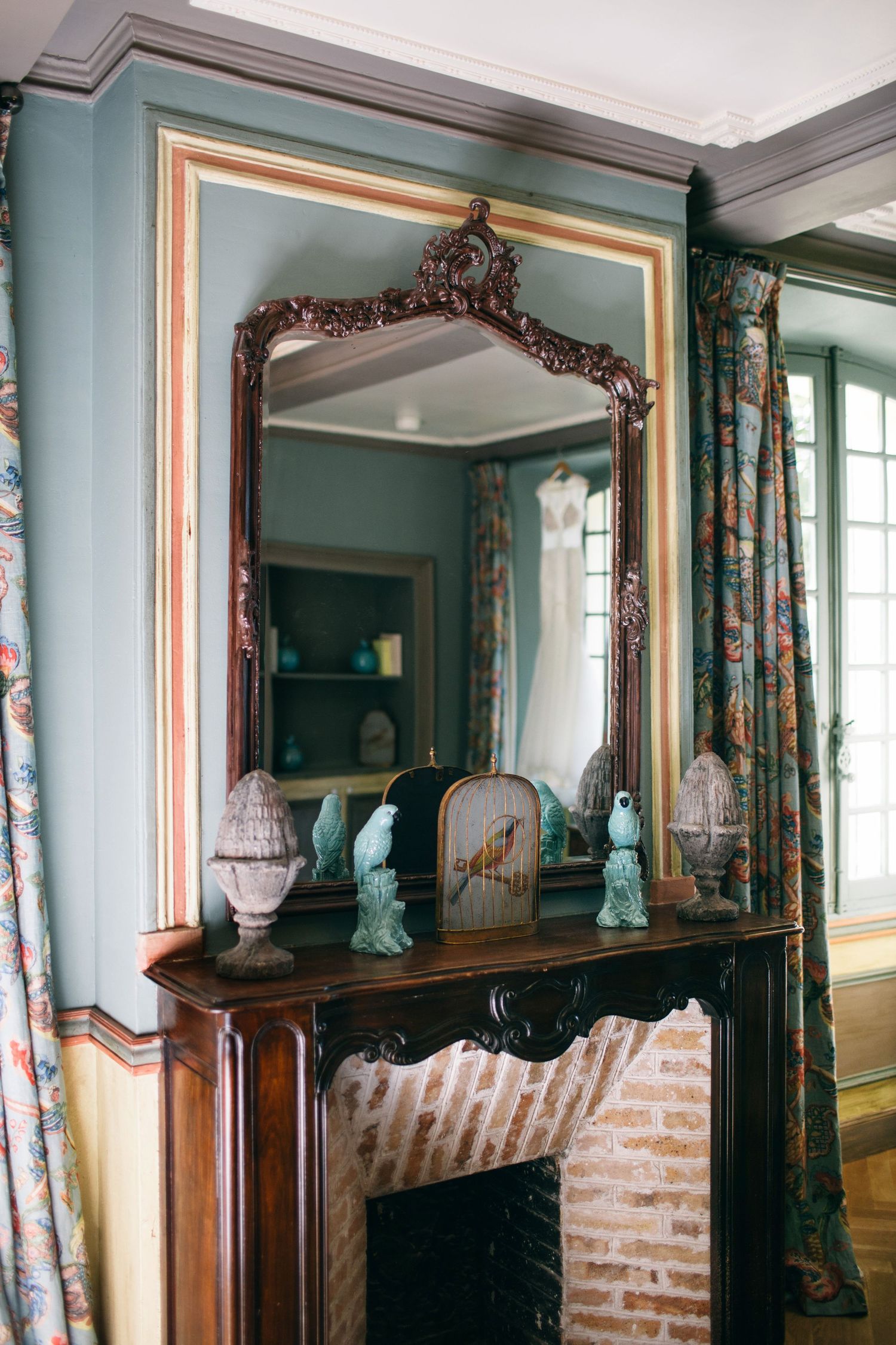 Ornate vintage mirror and decorative items on a wooden mantle in a teal-colored formal room.