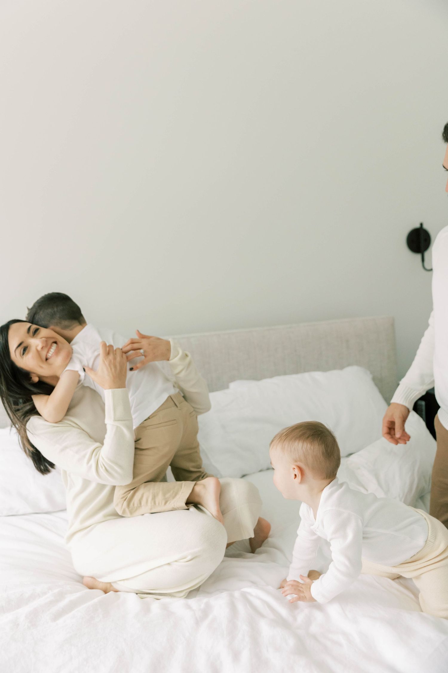 Family lounging together on white bed wearing matching light colored outfits.