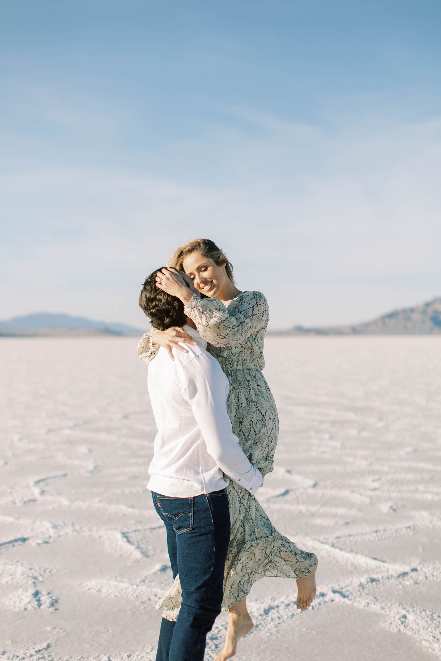A couple embracing on the stark white salt flats under a blue desert sky.