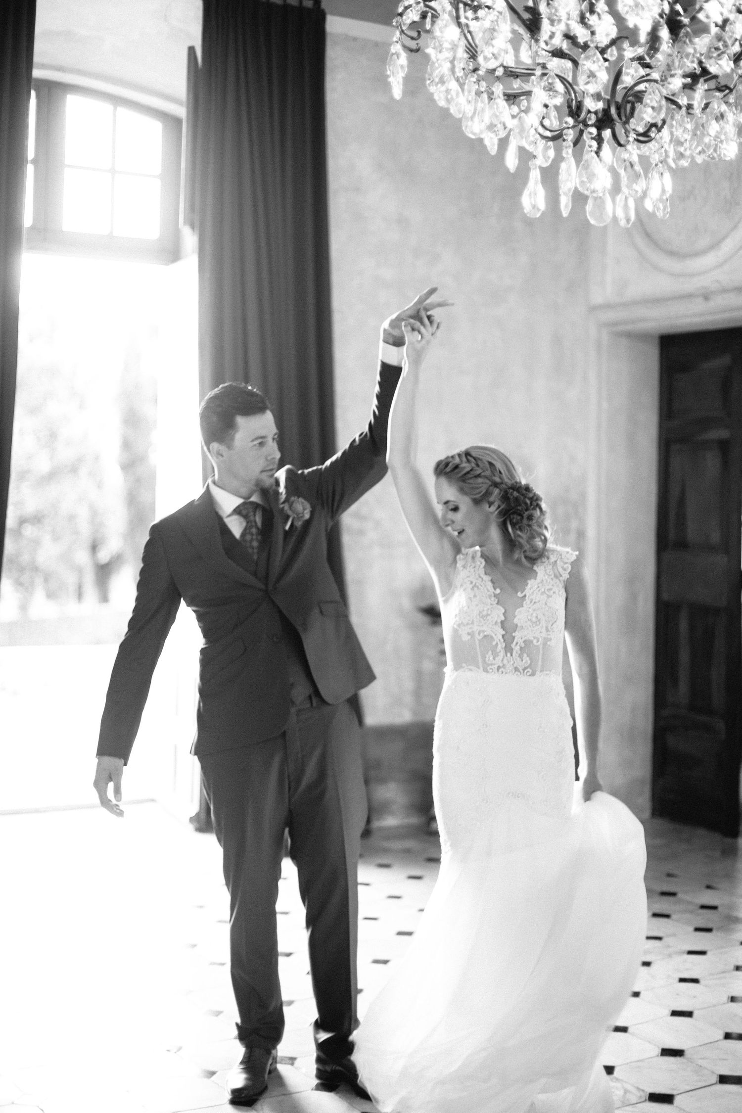 Wedding couple dancing playfully under a sparkling chandelier in an elegant room at chateau de moissac.