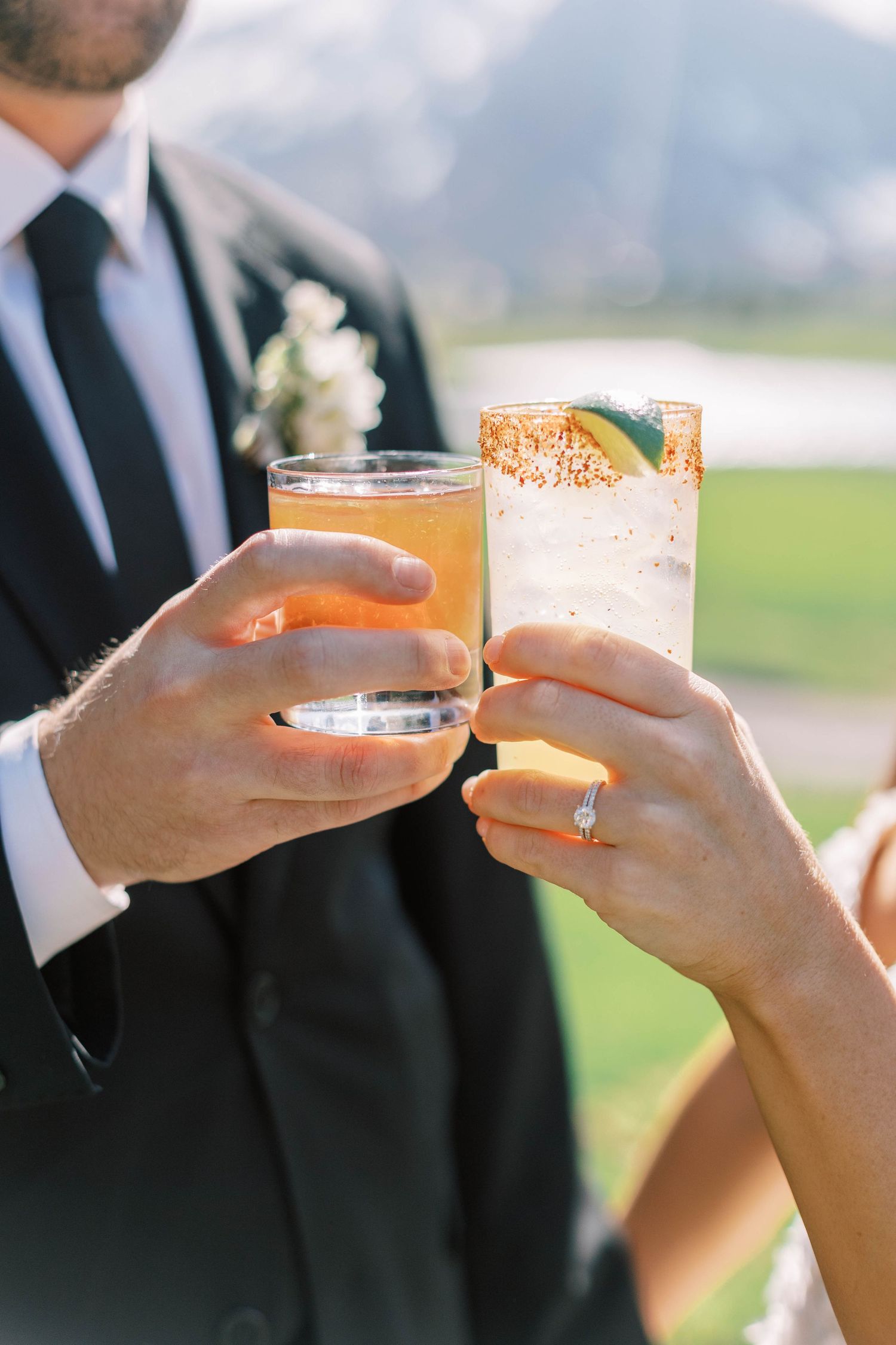 Wedding toast with cocktail glasses against mountain landscape.