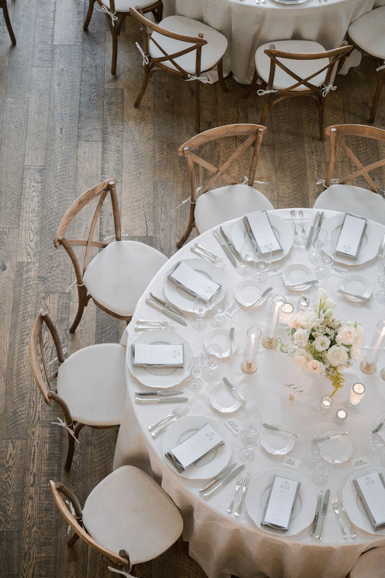 Elegant wedding reception tables set with white linens, cross-back chairs, and delicate floral centerpieces in a rustic venue.