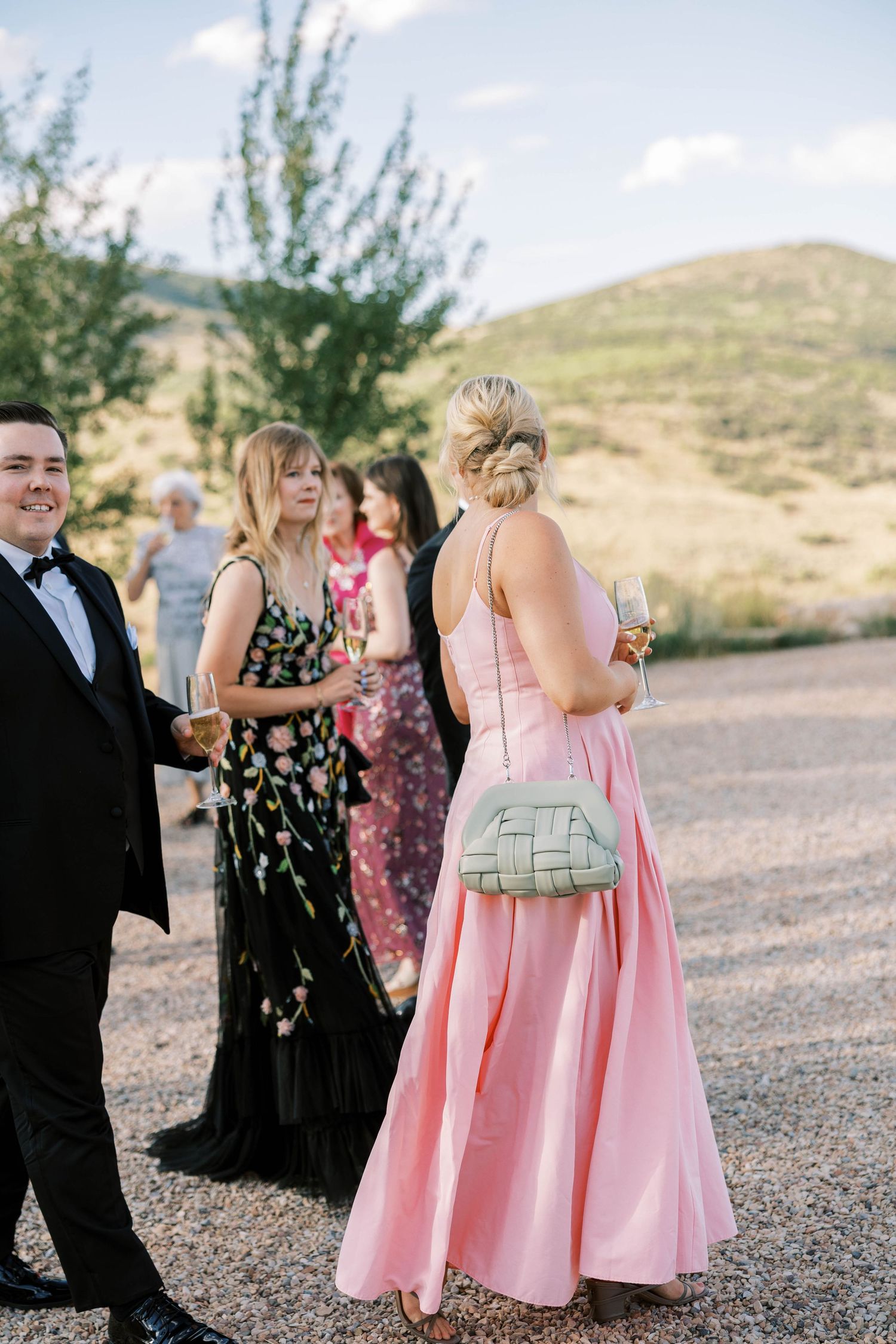 Wedding party in pink and floral dresses mingling at outdoor mountain ceremony.