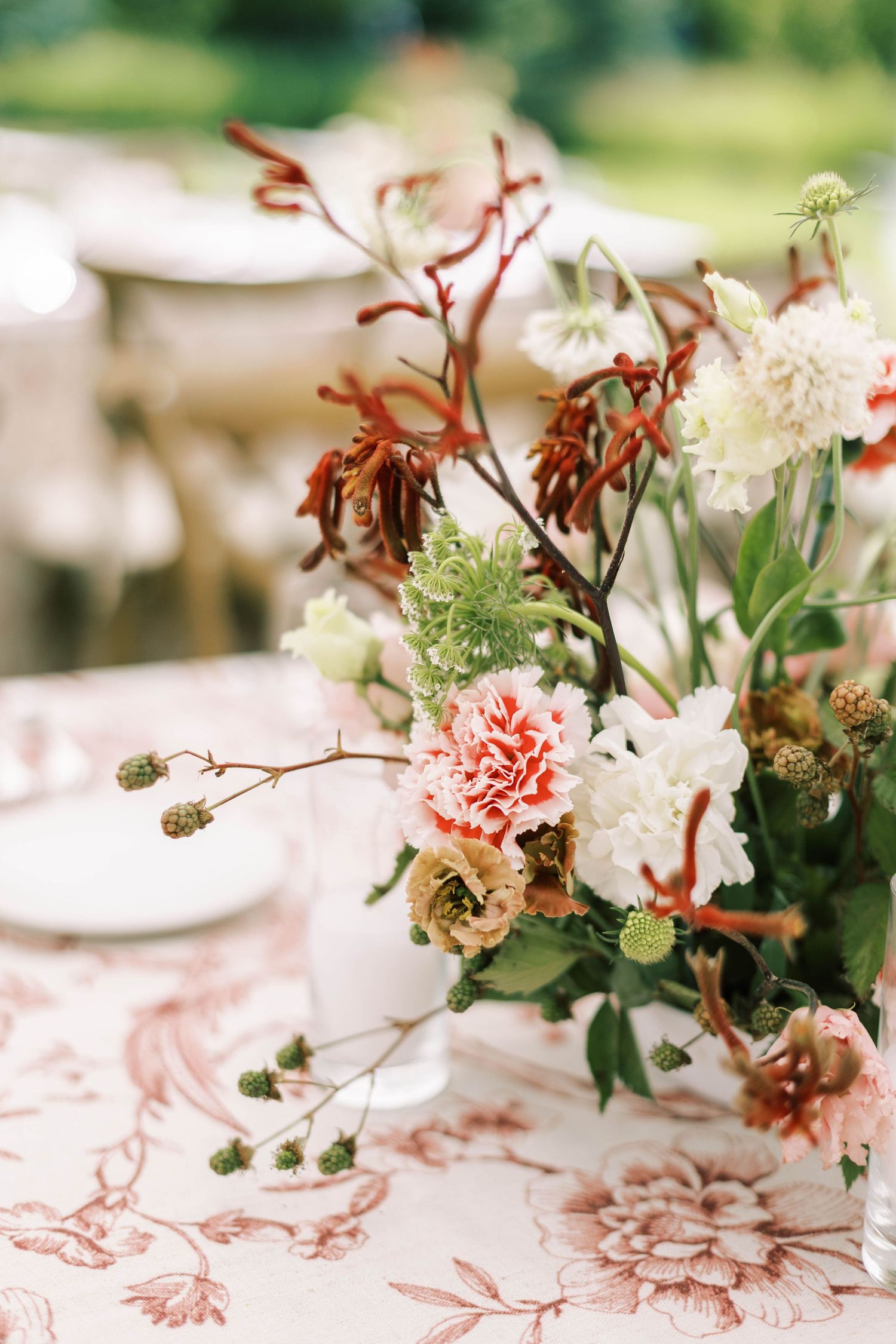 Elegant floral table centerpieces with pink carnations and white flowers on delicate toile patterned linens.