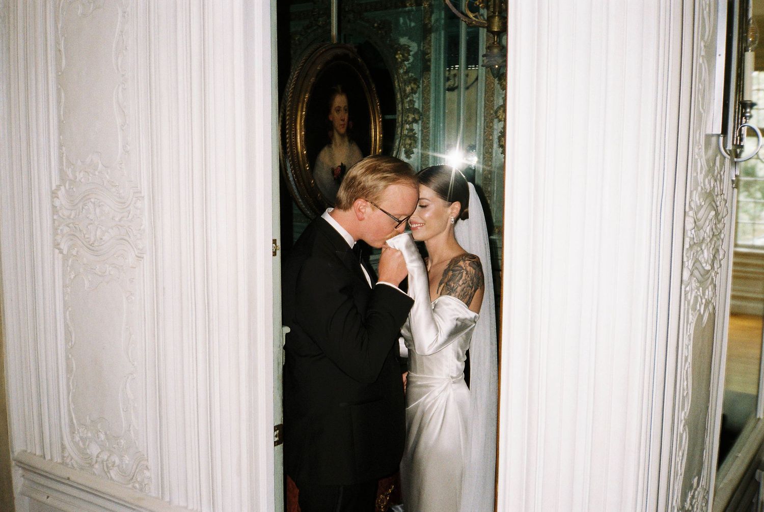 Romantic couple sharing intimate kisses in an elegant white hallway with ornate architectural details.