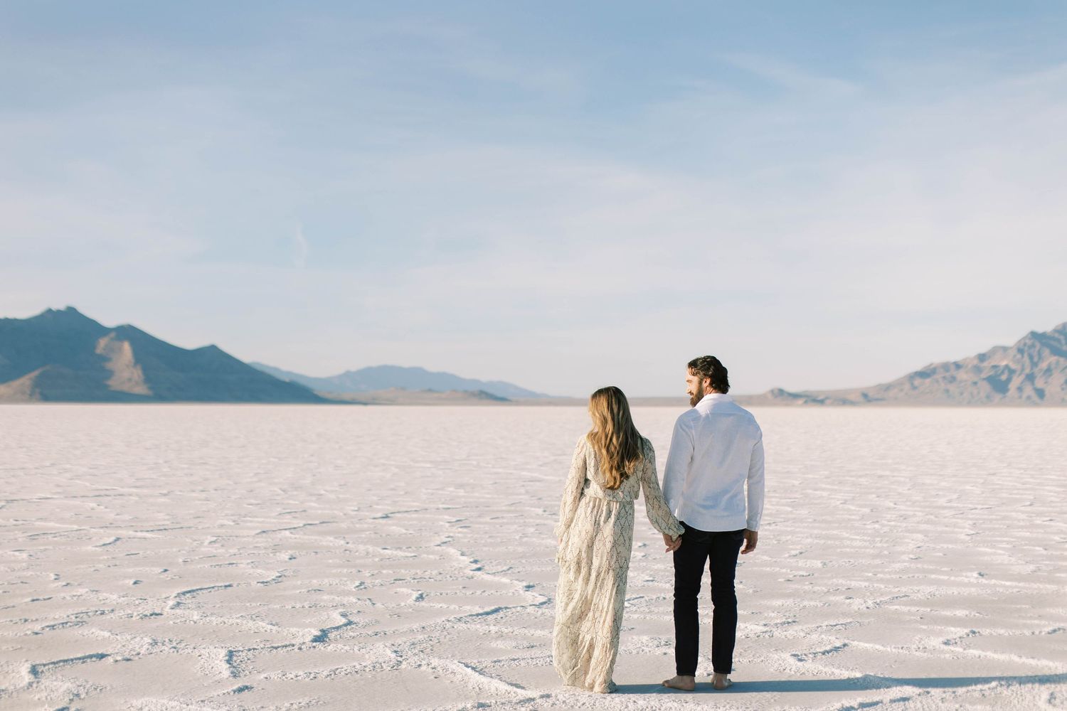 A couple stands together on the vast white Utah salt flats with mountains in the distance.