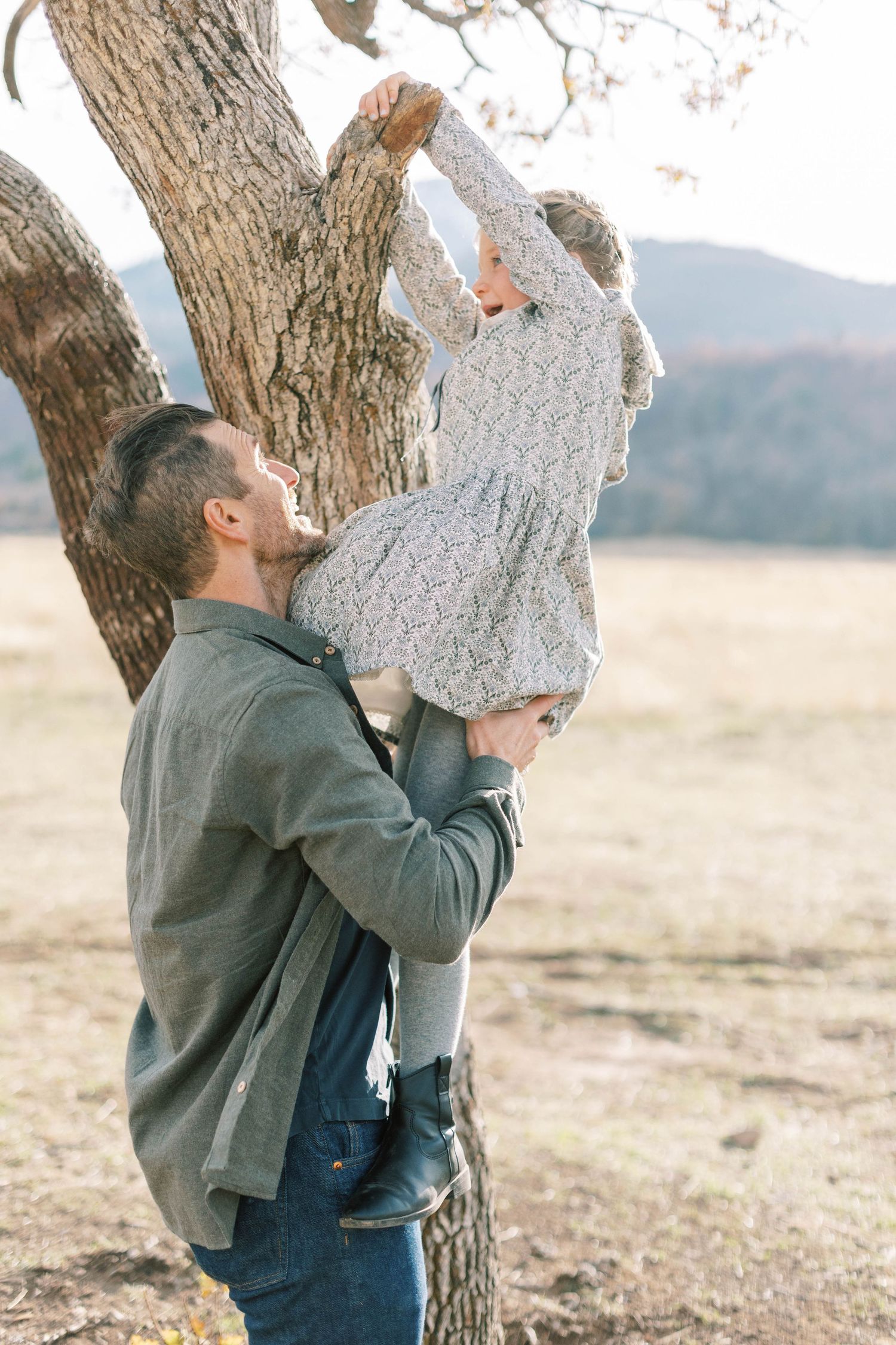 Adult lifting child up to tree branches in mountain field during autumn.