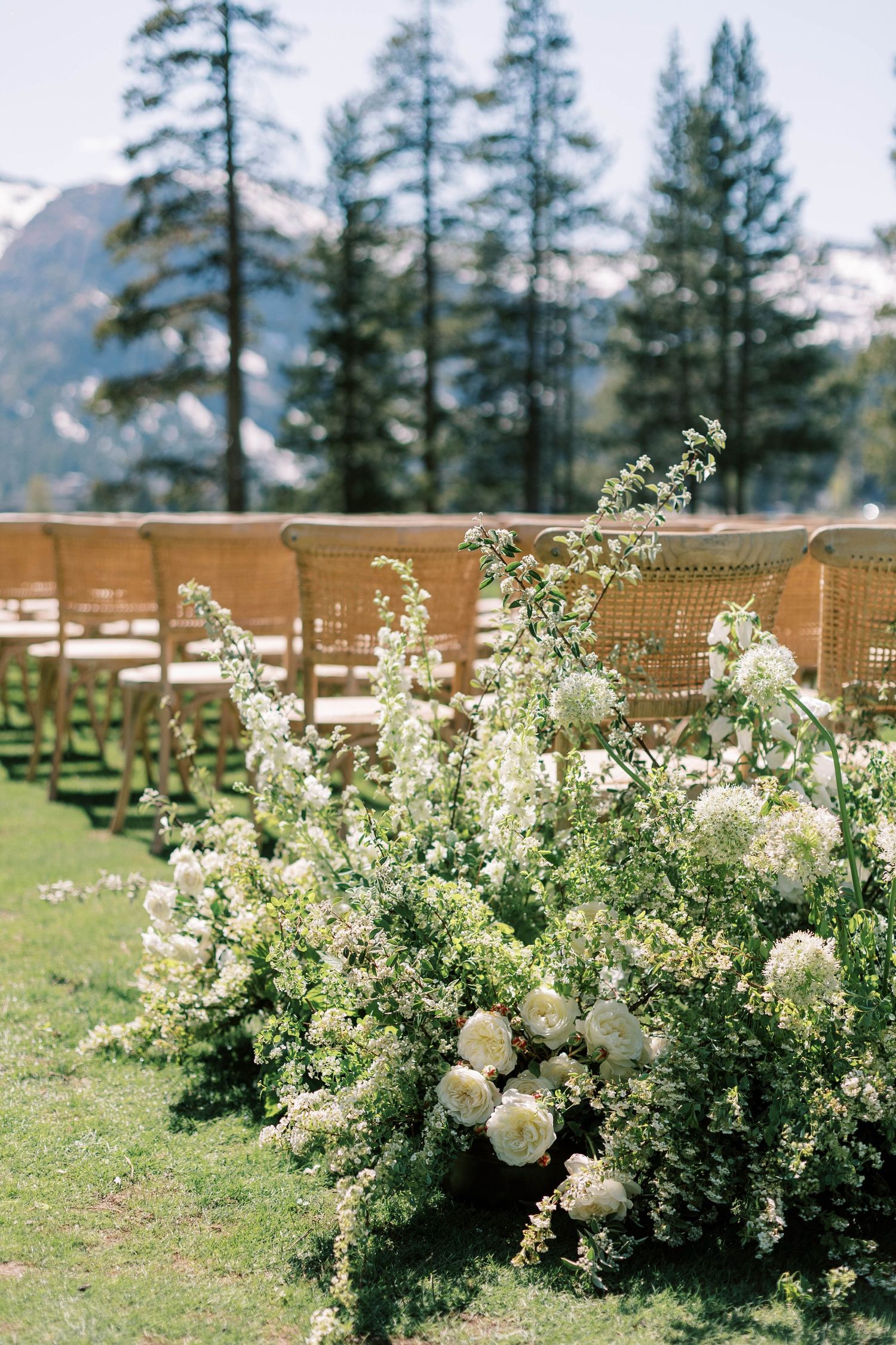 Elegant white floral arrangements line wooden chairs at outdoor mountain wedding venue at everline resort in lake tahoe.
