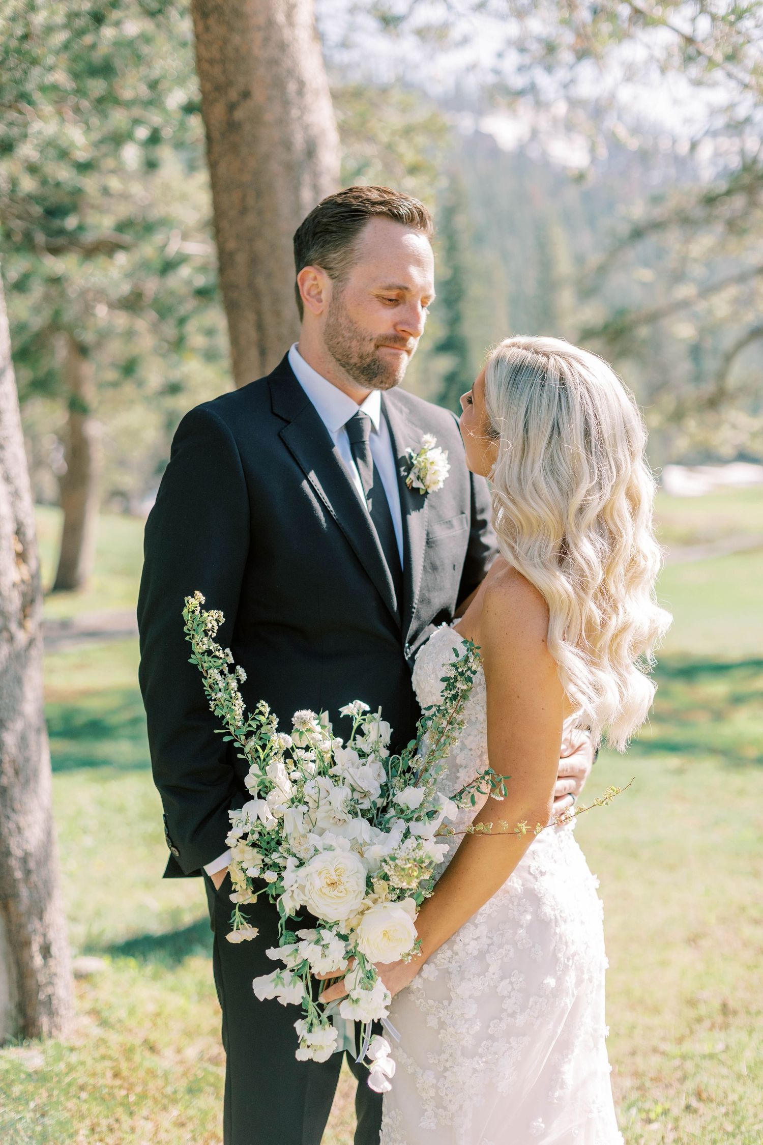 Elegant wedding portrait with white floral bouquet against mountain scenery.