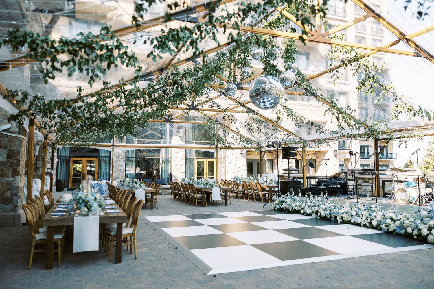 Elegant greenhouse wedding reception venue with checkered floor, wooden chairs and hanging greenery decorations.