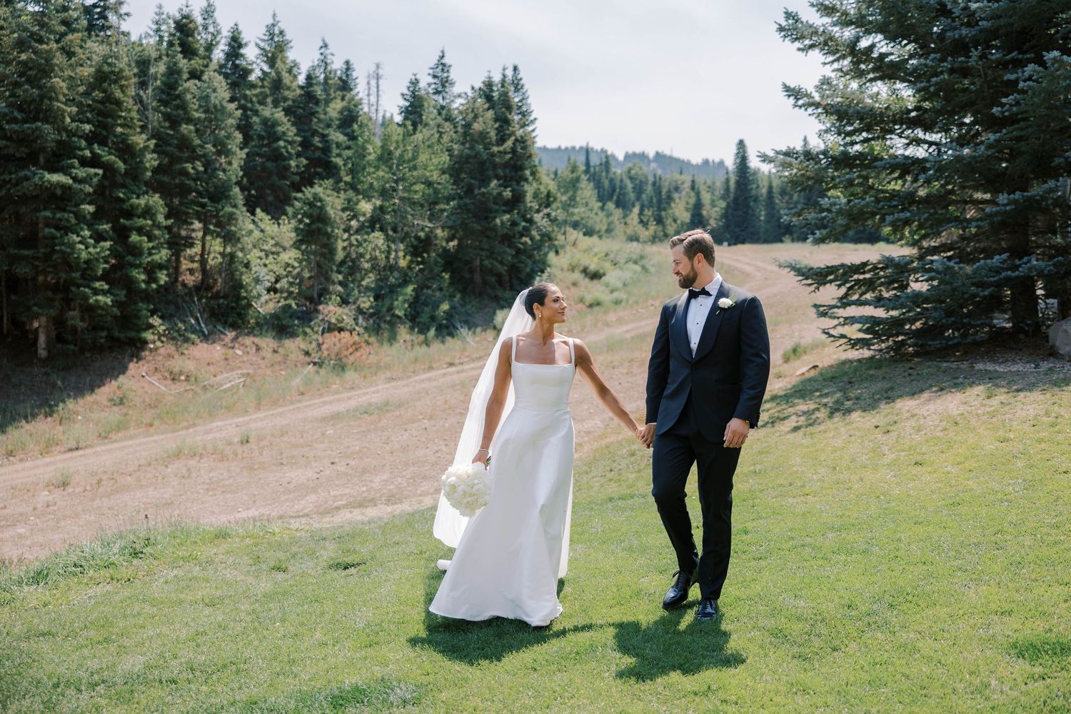 Romantic wedding photography session on a scenic mountain meadow with pine trees in the background.